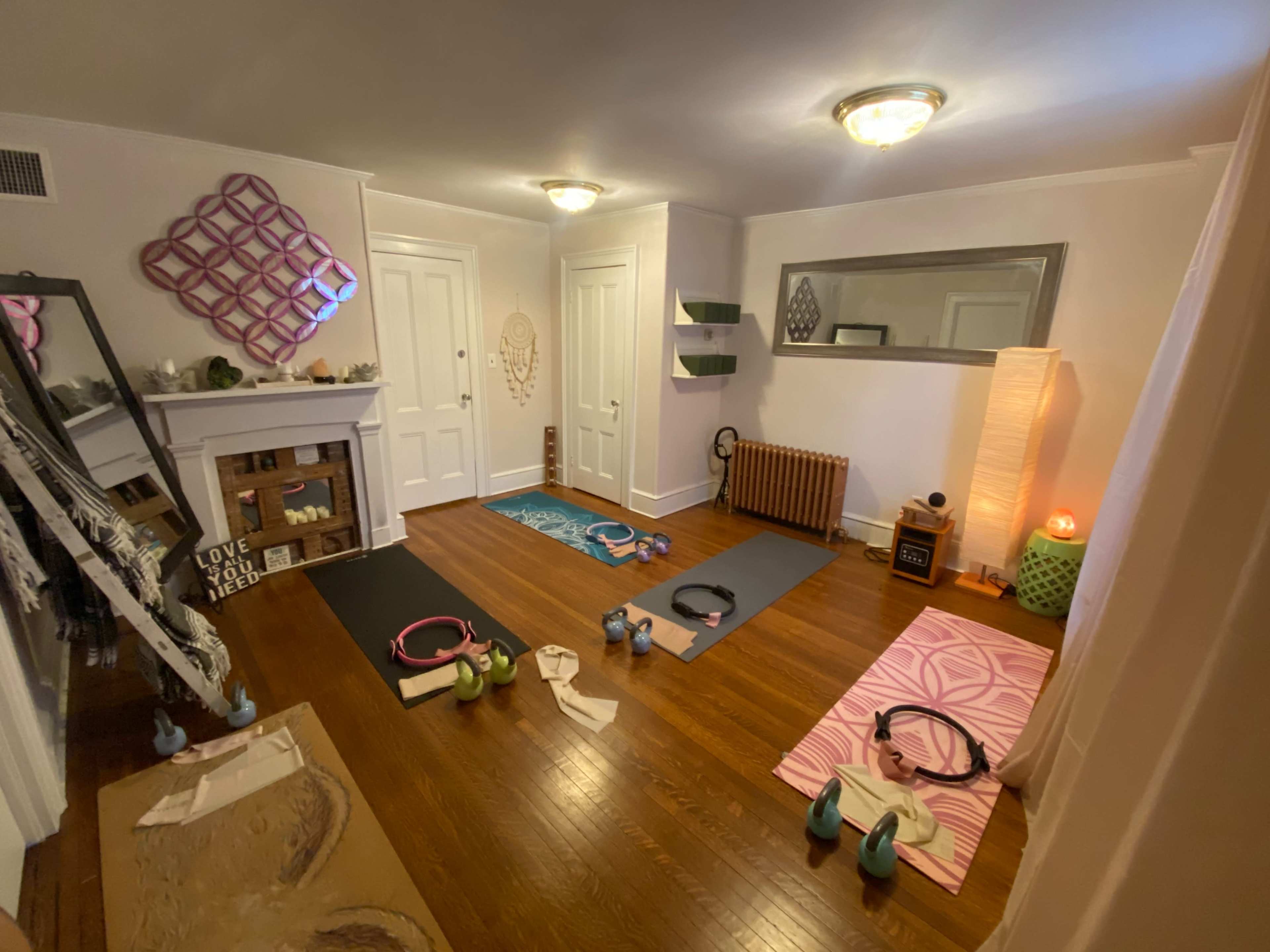 A brightly lit exercise room features yoga mats, weights, a mirror, and decorative elements, creating a space for physical activity.