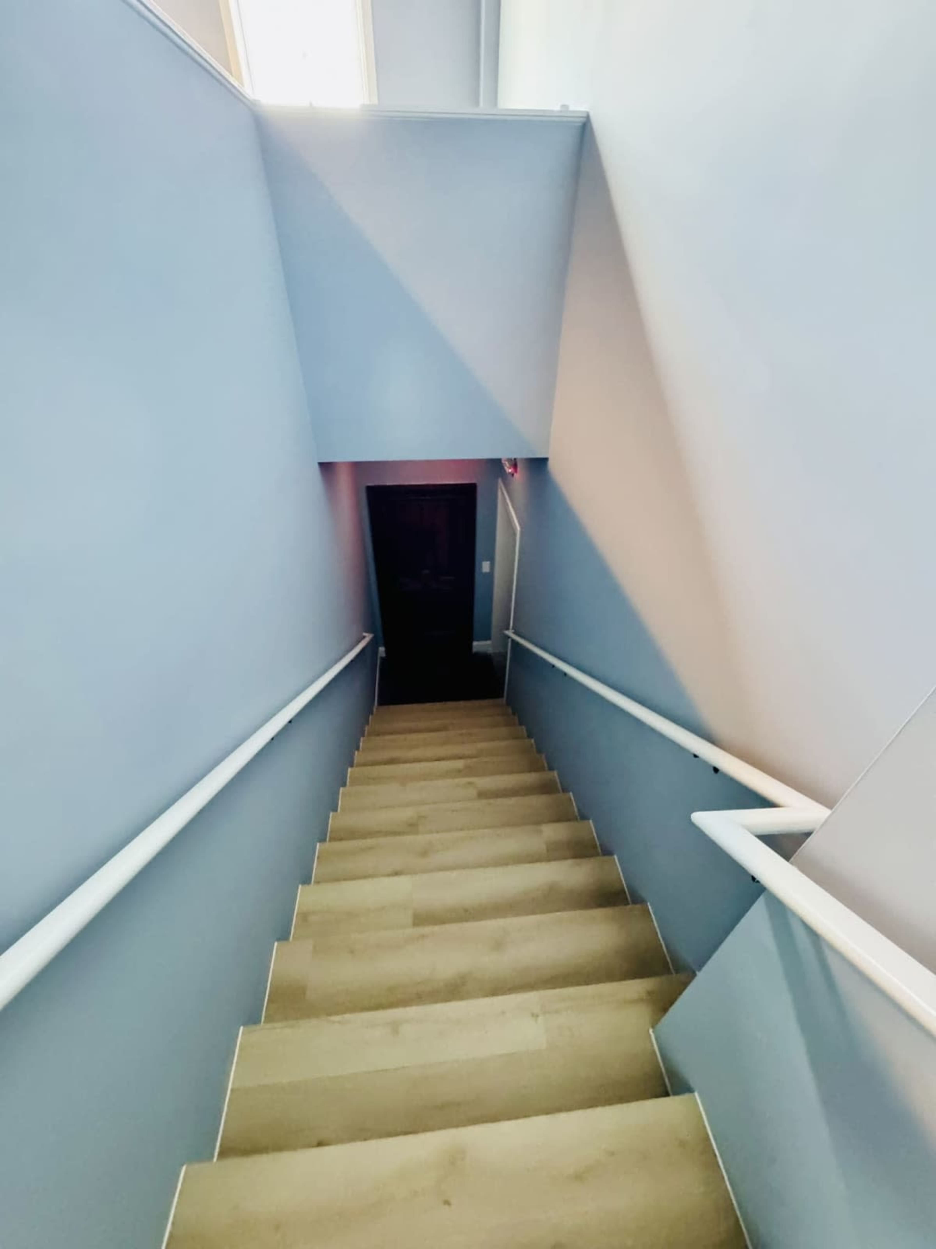 The image shows a staircase leading down to a door at the bottom, surrounded by light blue walls.