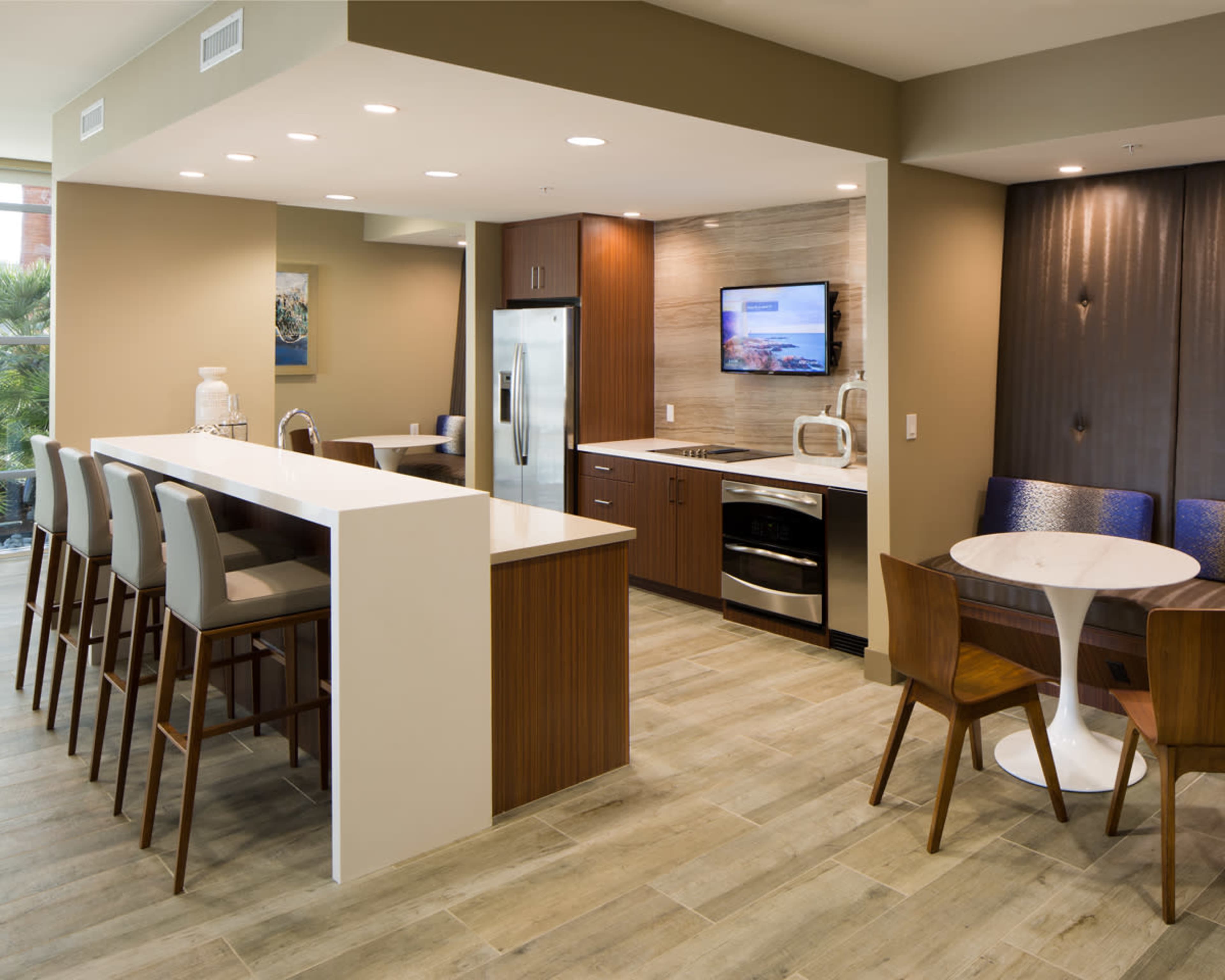 A modern kitchen area features a central island with bar stools, stainless steel appliances, and a dining table in a well-lit, open layout.