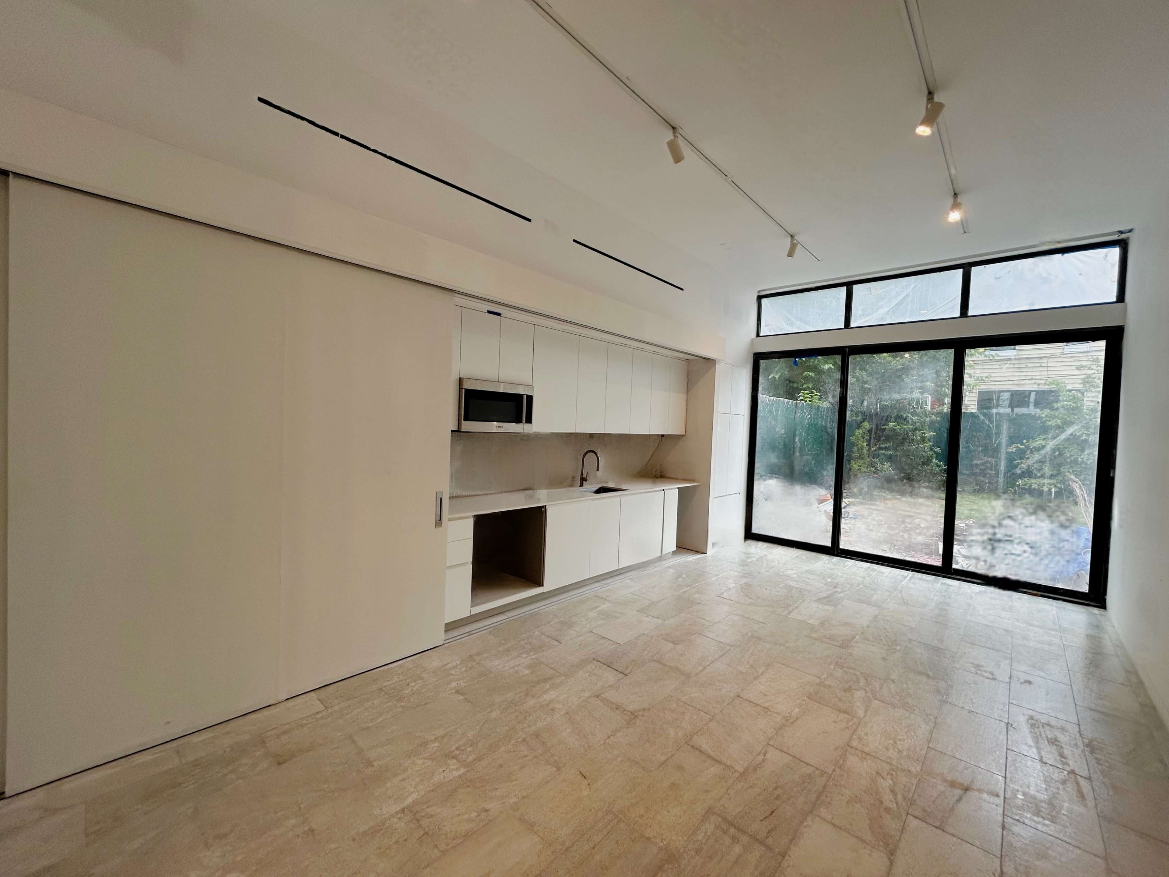 The image shows a modern kitchen space with a sliding door, marble flooring, and large windows that overlook a garden.
