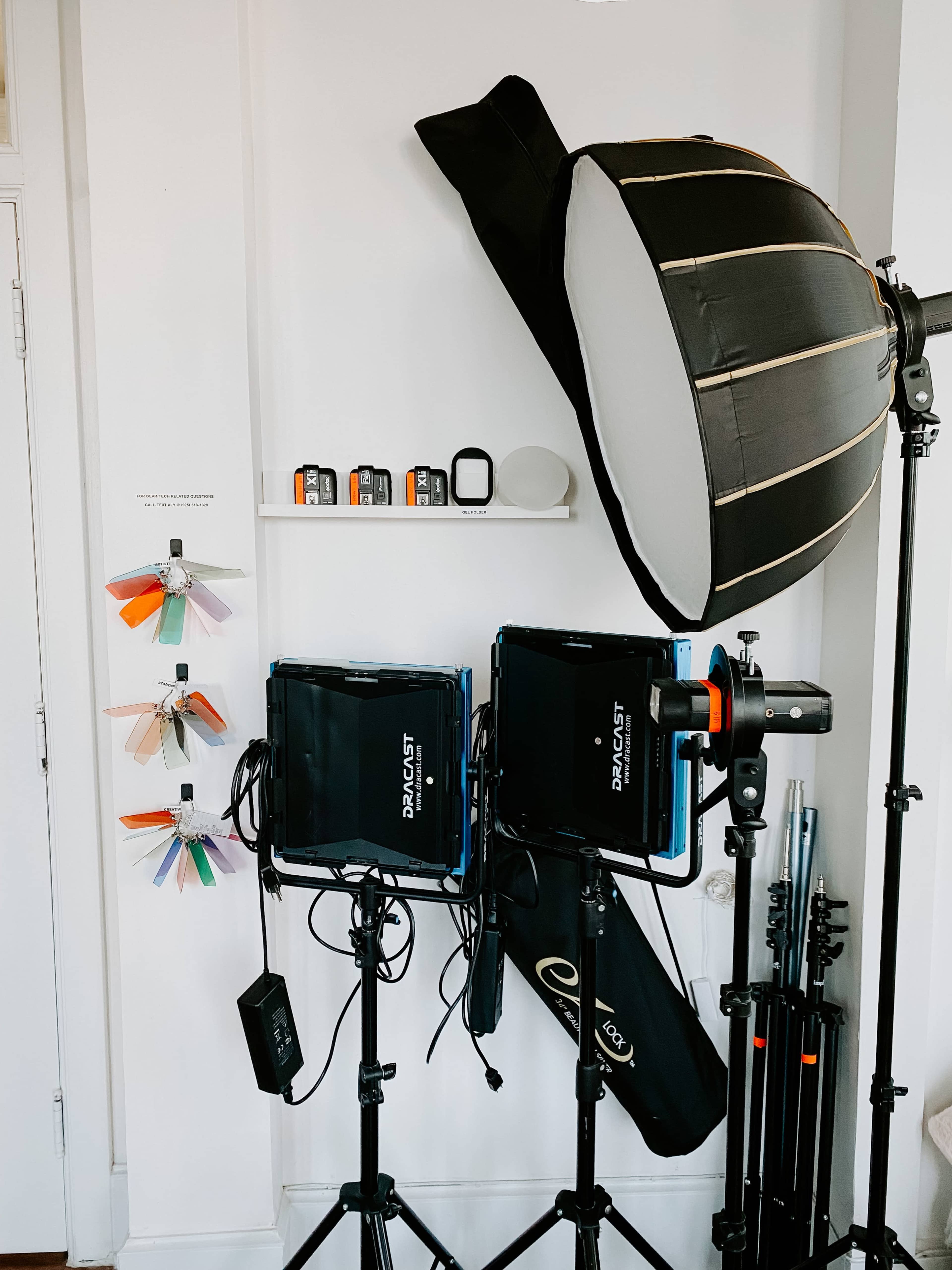 A photography setup with two softbox lights on stands, a light meter, and a shelf displaying color samples and equipment.