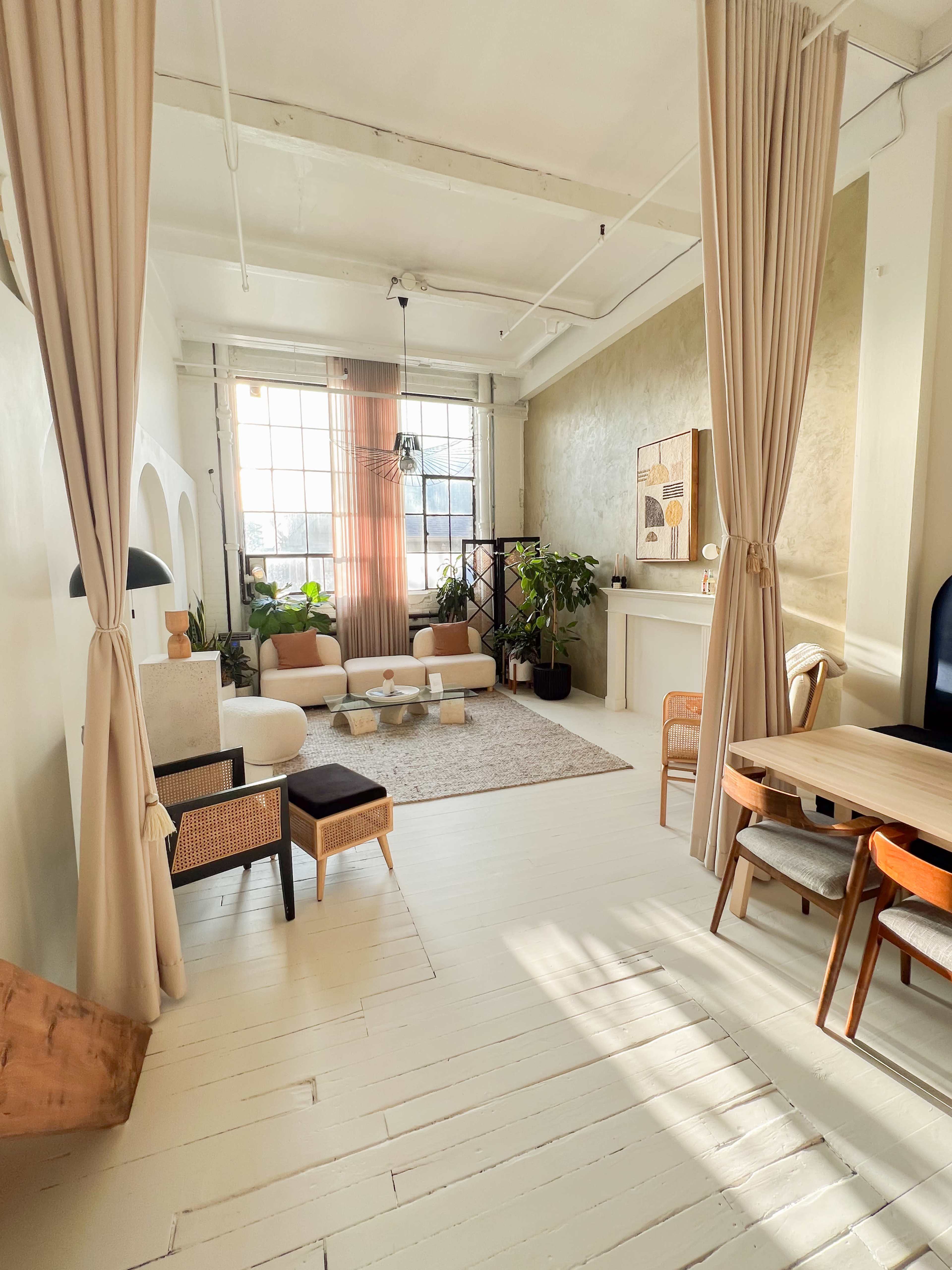 A bright, modern living space with light-colored walls, a large window, and a mix of seating options, including a round coffee table and a dining area.