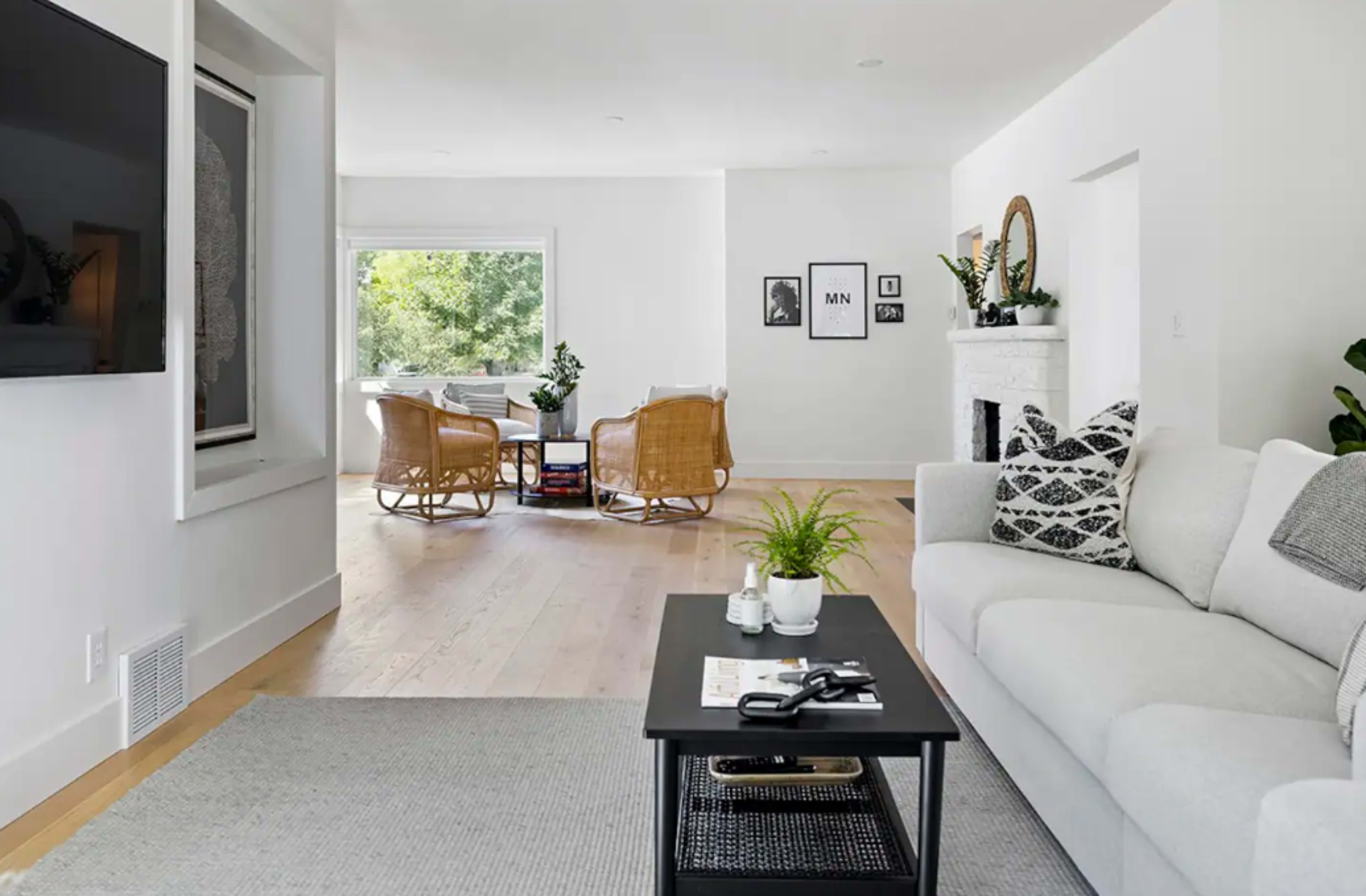 A modern living room features a light-colored sofa, a black coffee table, and wicker chairs arranged around a bright window.