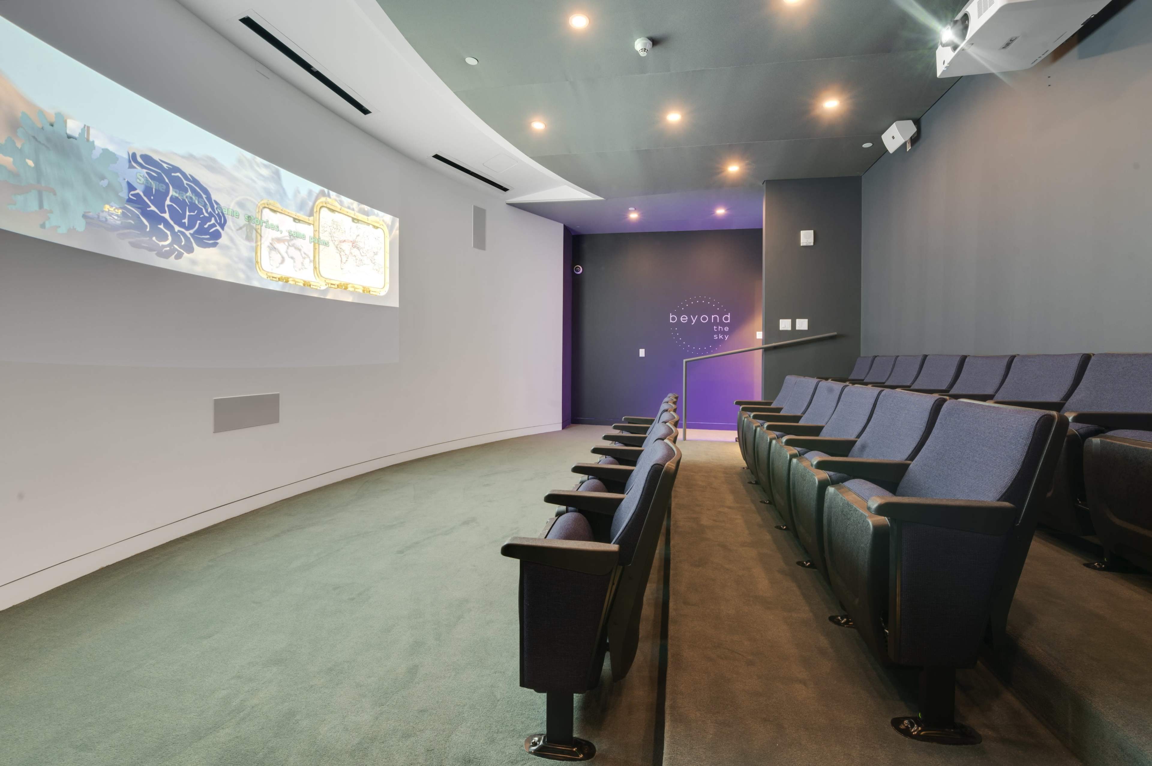 A small, modern theater with tiered seating and a large screen displaying animated visuals on one wall.