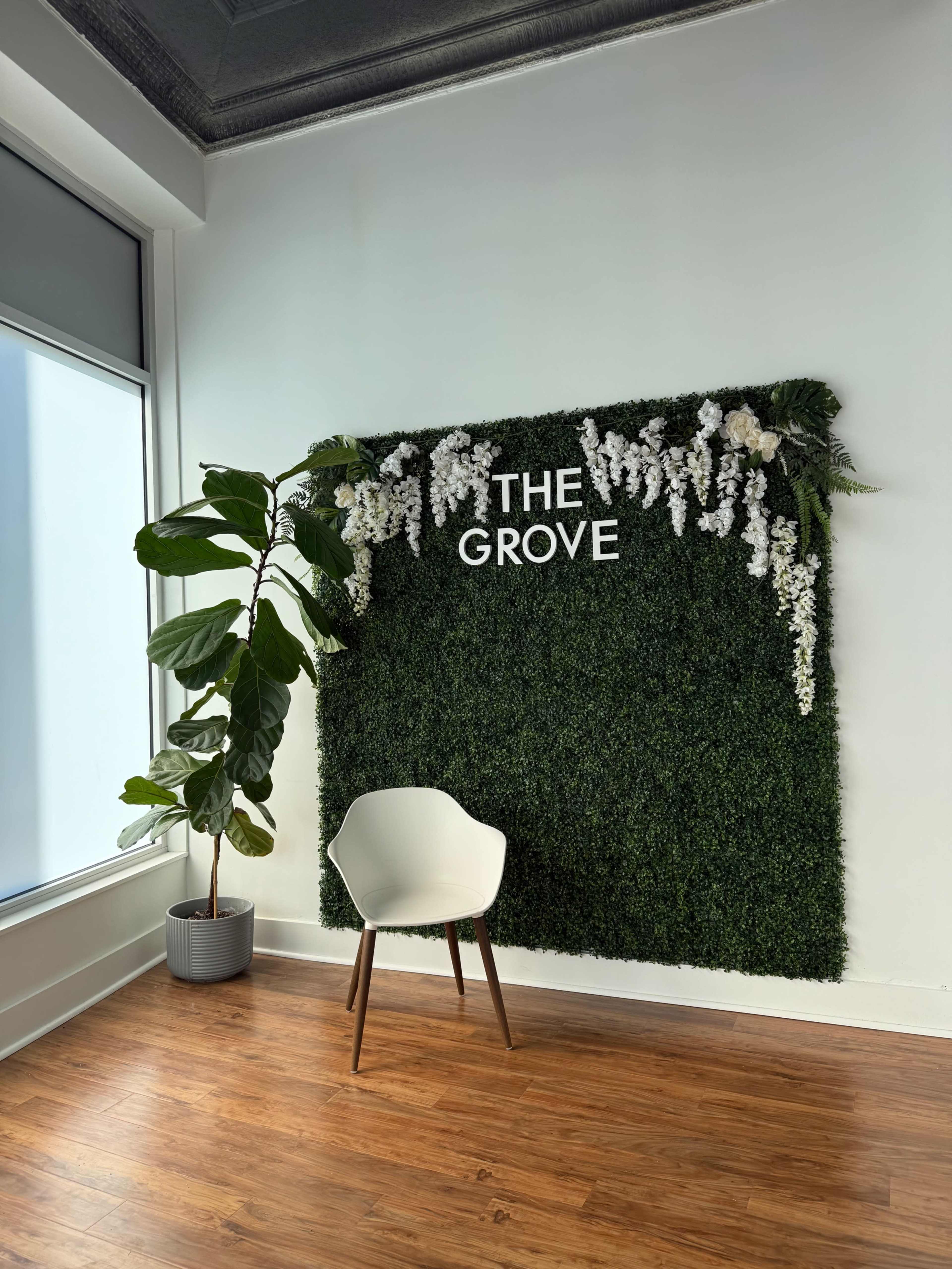 The image shows a modern interior with a green wall adorned with white flowers and the text "THE GROVE," accompanied by a potted plant and a white chair on a wooden floor.