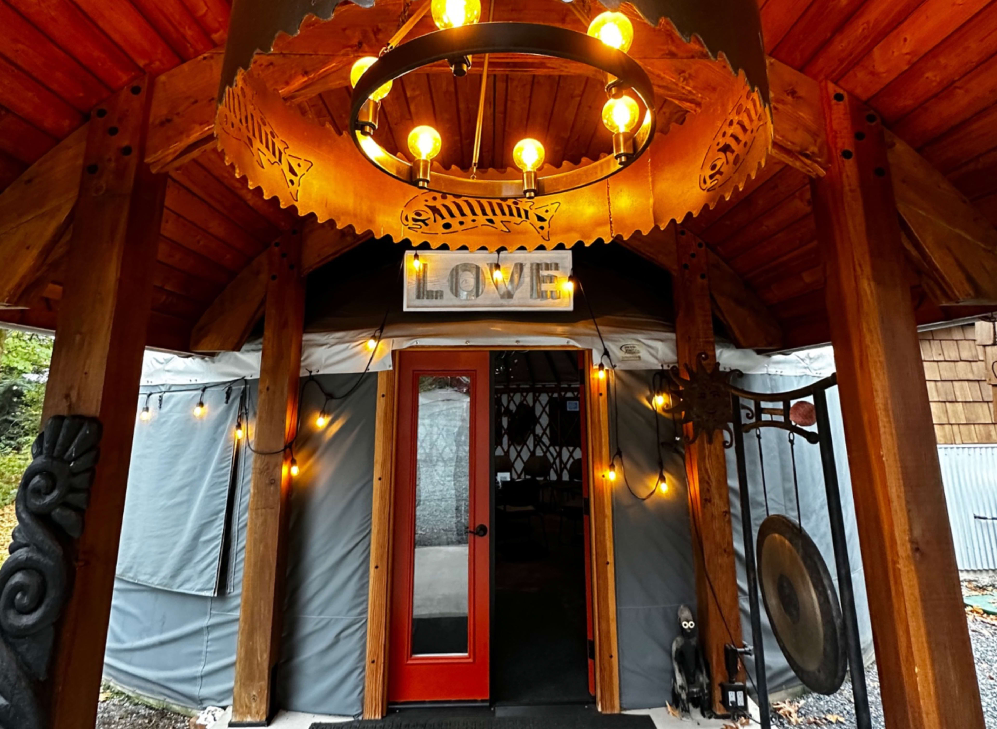 The entrance of a yurt adorned with a circular chandelier and string lights, featuring a red door and a sign that reads "LOVE."