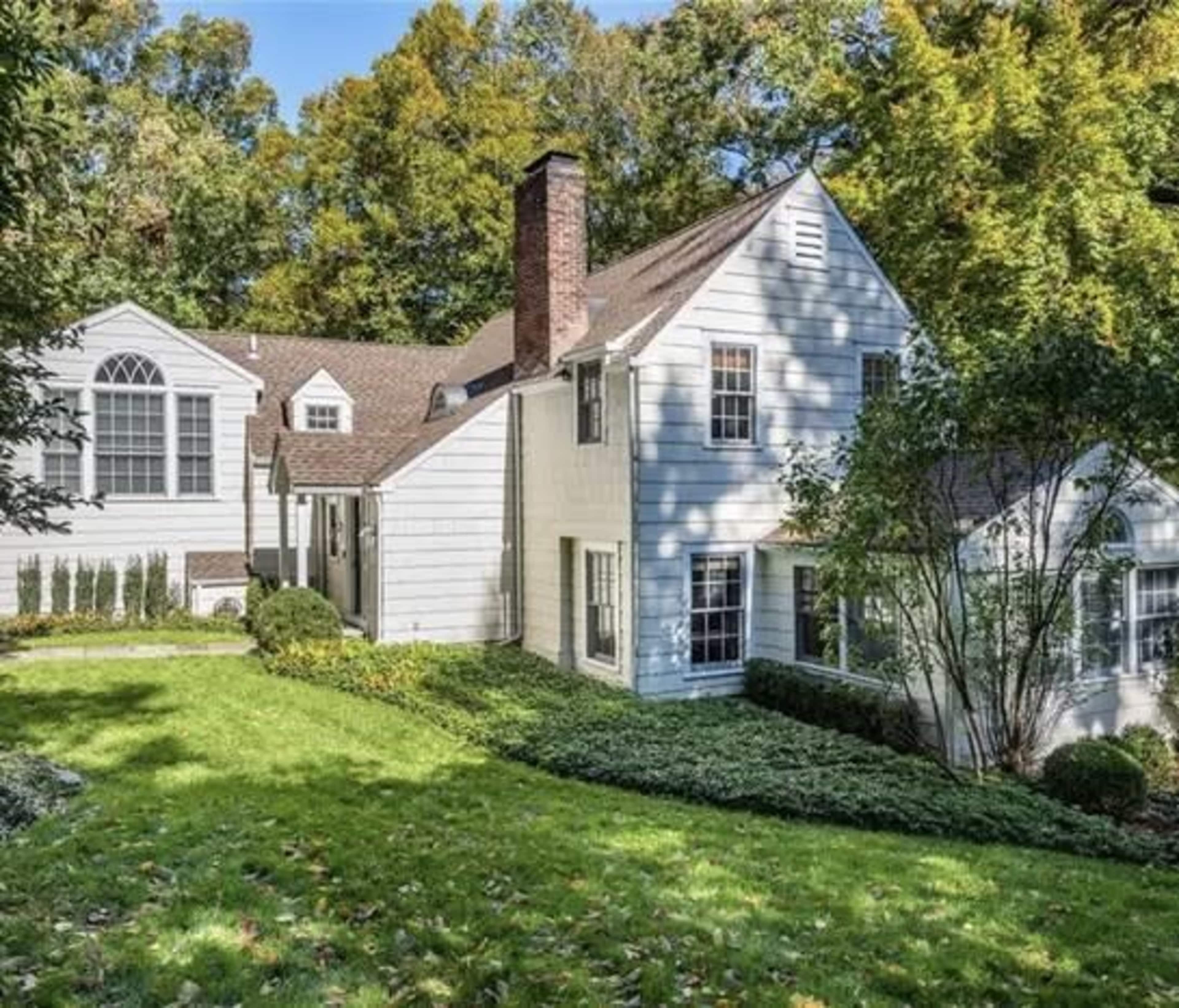 A two-story, white house surrounded by trees and a landscaped yard.