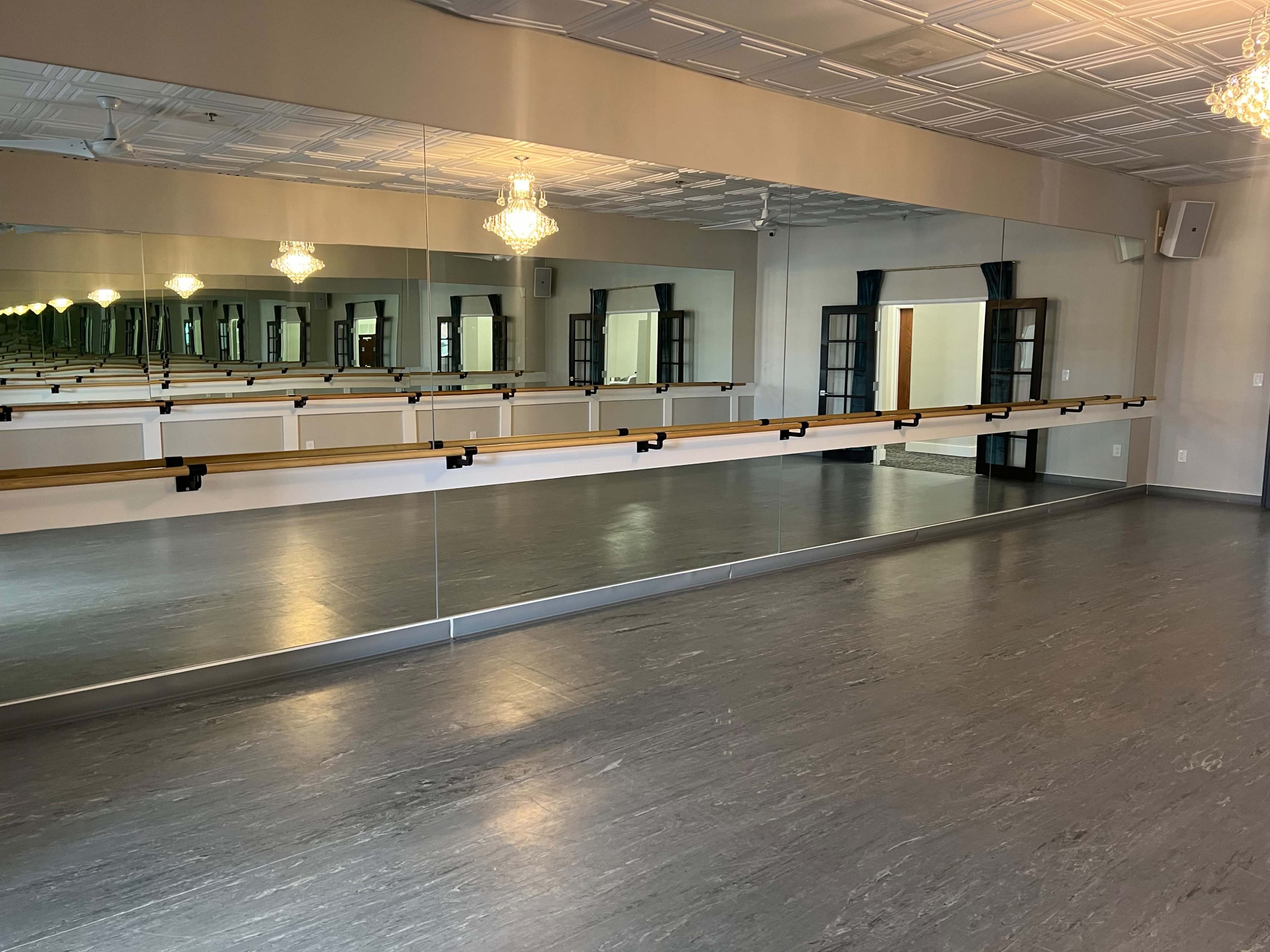 A ballet studio with wooden barres along the mirrored wall and a gray floor.