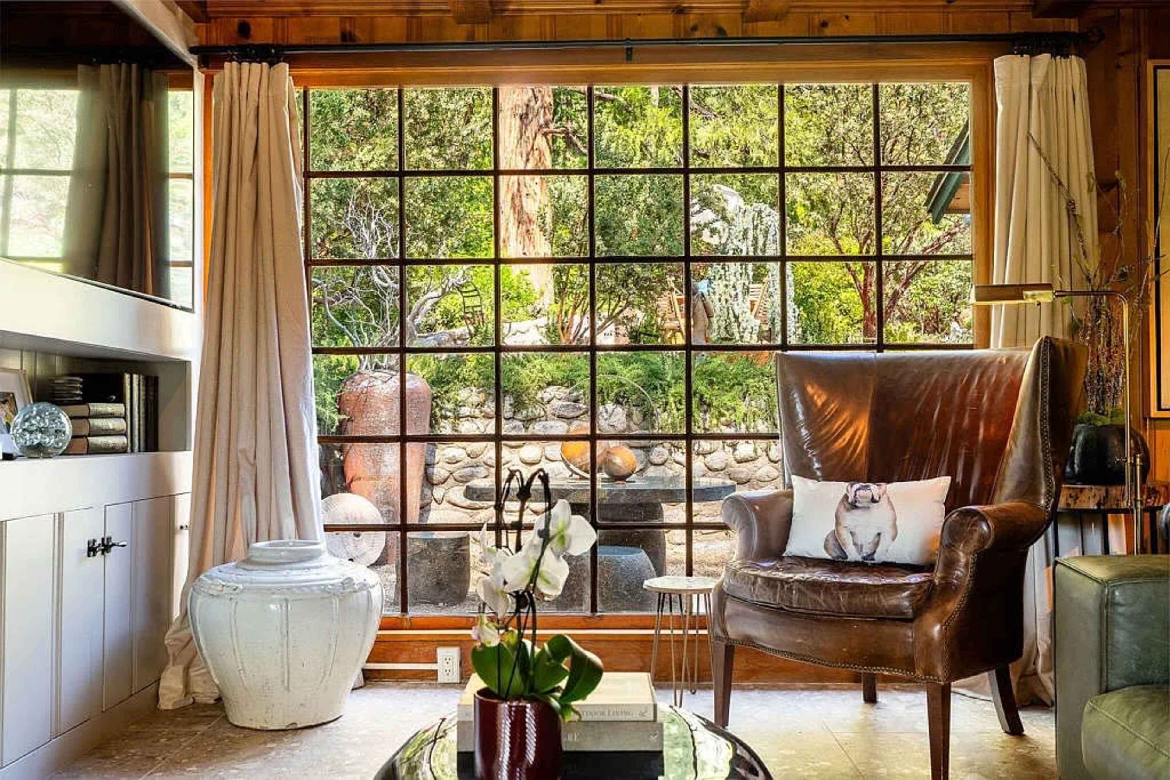 A cozy seating area features a large window overlooking a landscaped garden with stone features and greenery.