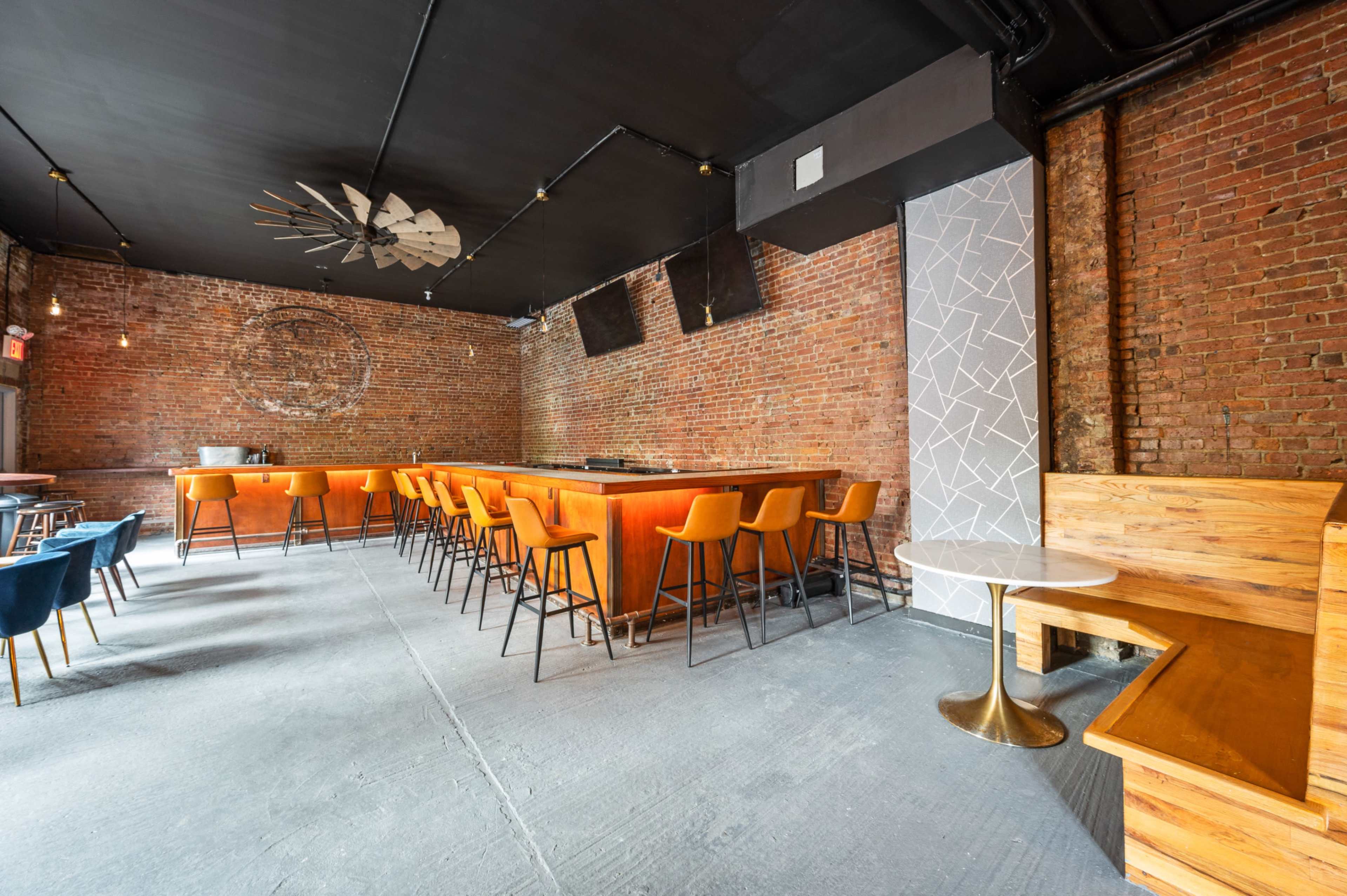 A spacious bar area with a wooden counter and orange stools, exposed brick walls, and a minimalist seating arrangement.
