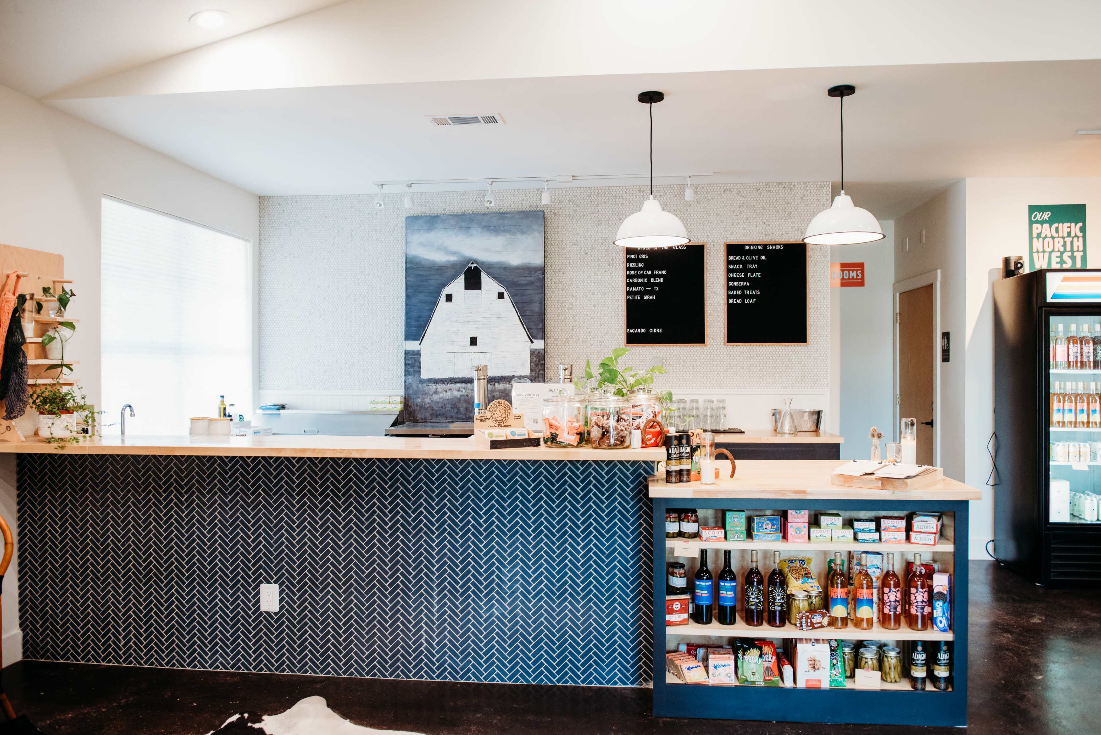 A modern café interior with a wooden counter, a large wall art piece, menu boards, and shelves displaying various beverages and snacks.