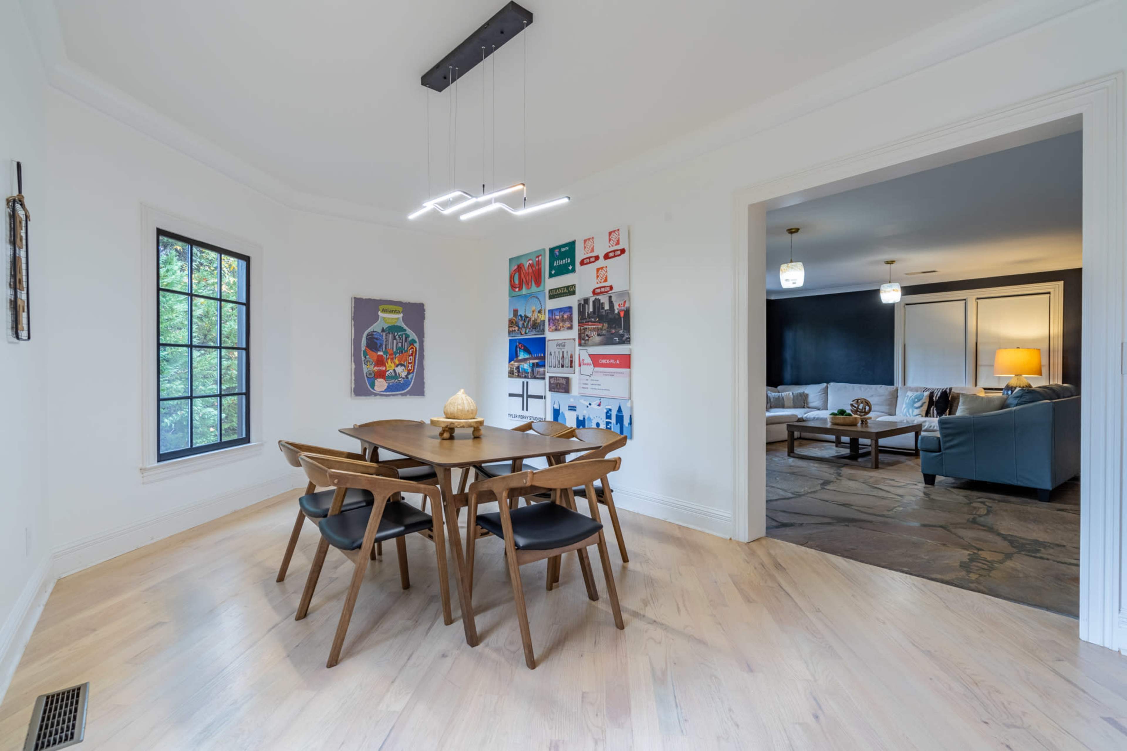 A dining area features a wooden table surrounded by black chairs, with artwork and promotional posters on the walls.