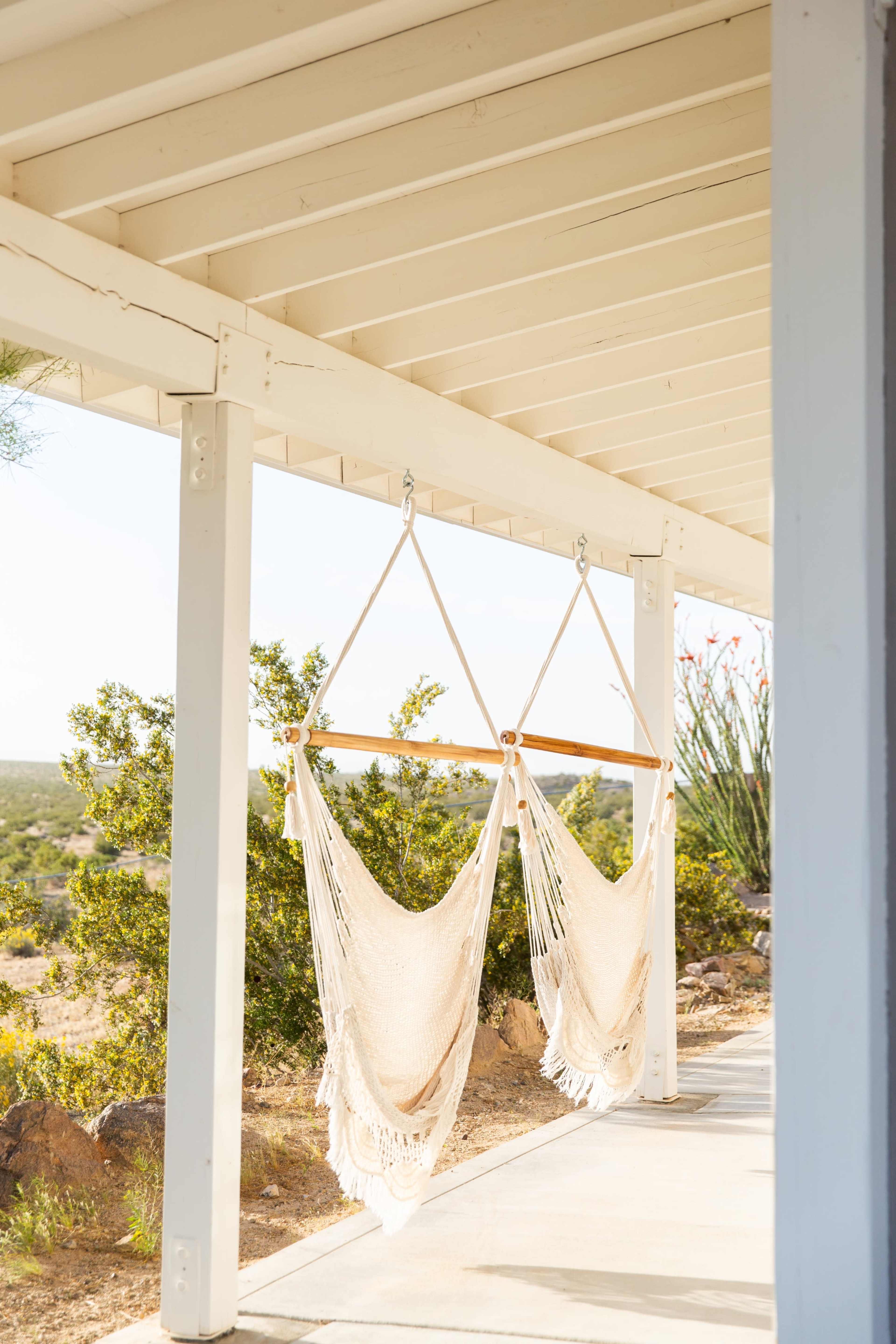 Two beige hammocks hang from a white porch ceiling, overlooking a desert landscape.
