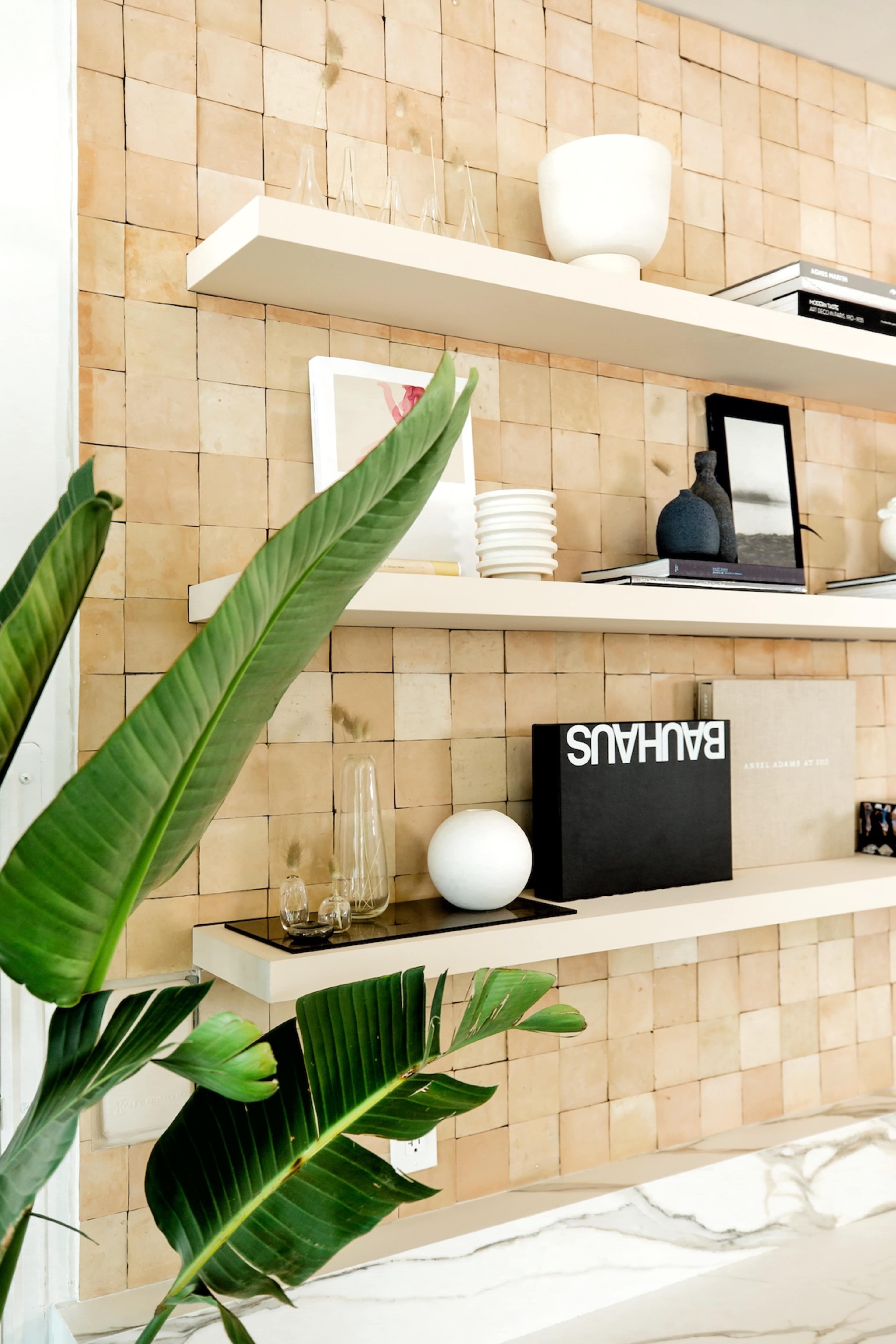 A modern shelf arrangement with decorative items and plants against a patterned wall.
