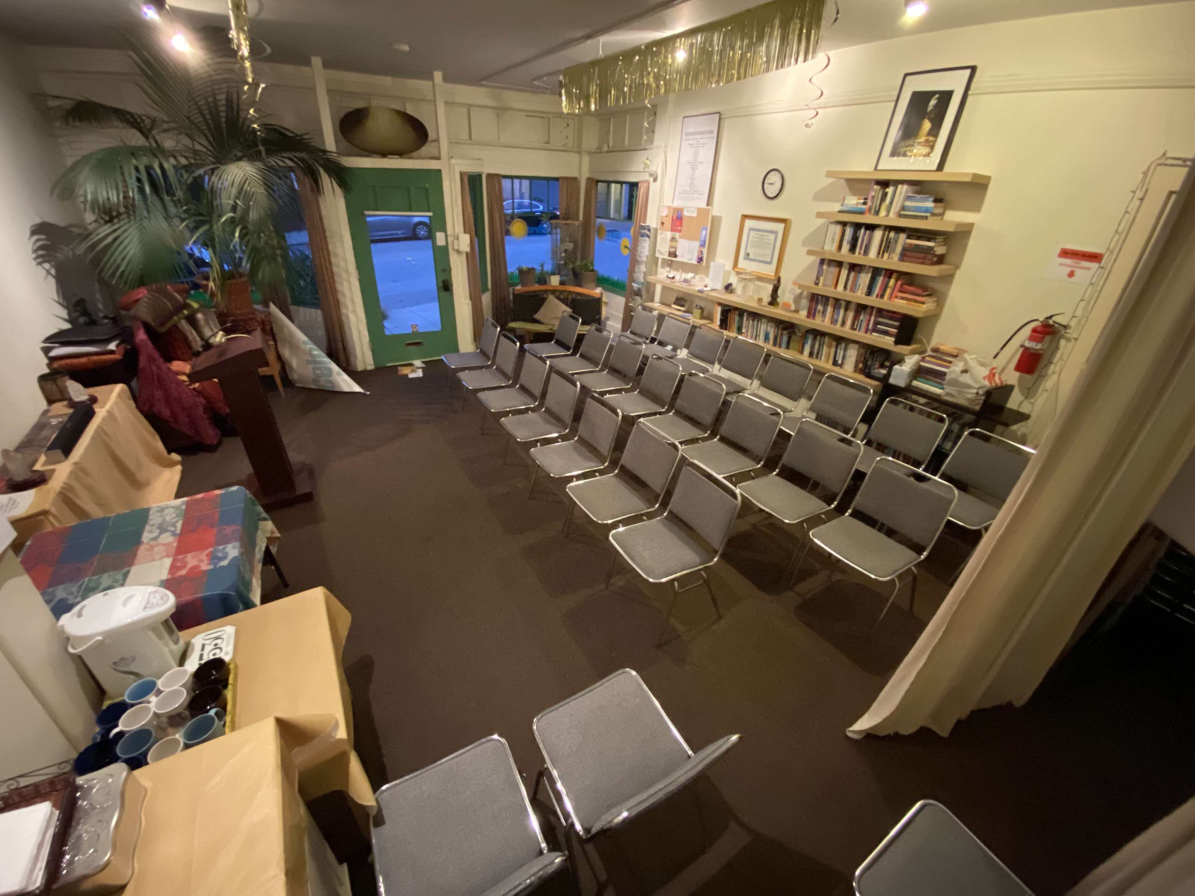 A room arranged with metal chairs facing a podium, adorned with decorations and bookshelves in the background.