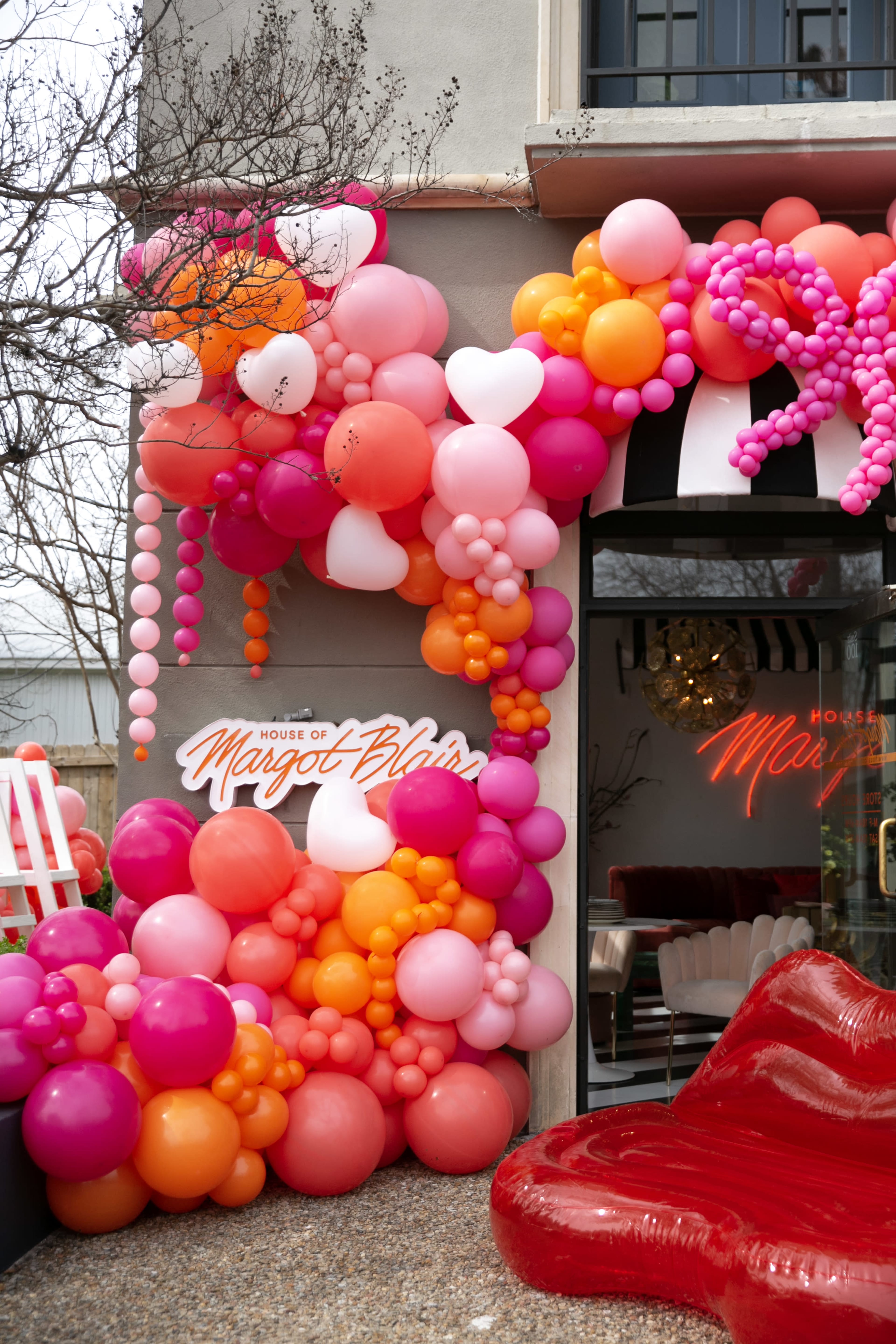 A colorful arrangement of balloons in shades of pink, orange, and white decorates the entrance of a building named "House of Margot Blair."