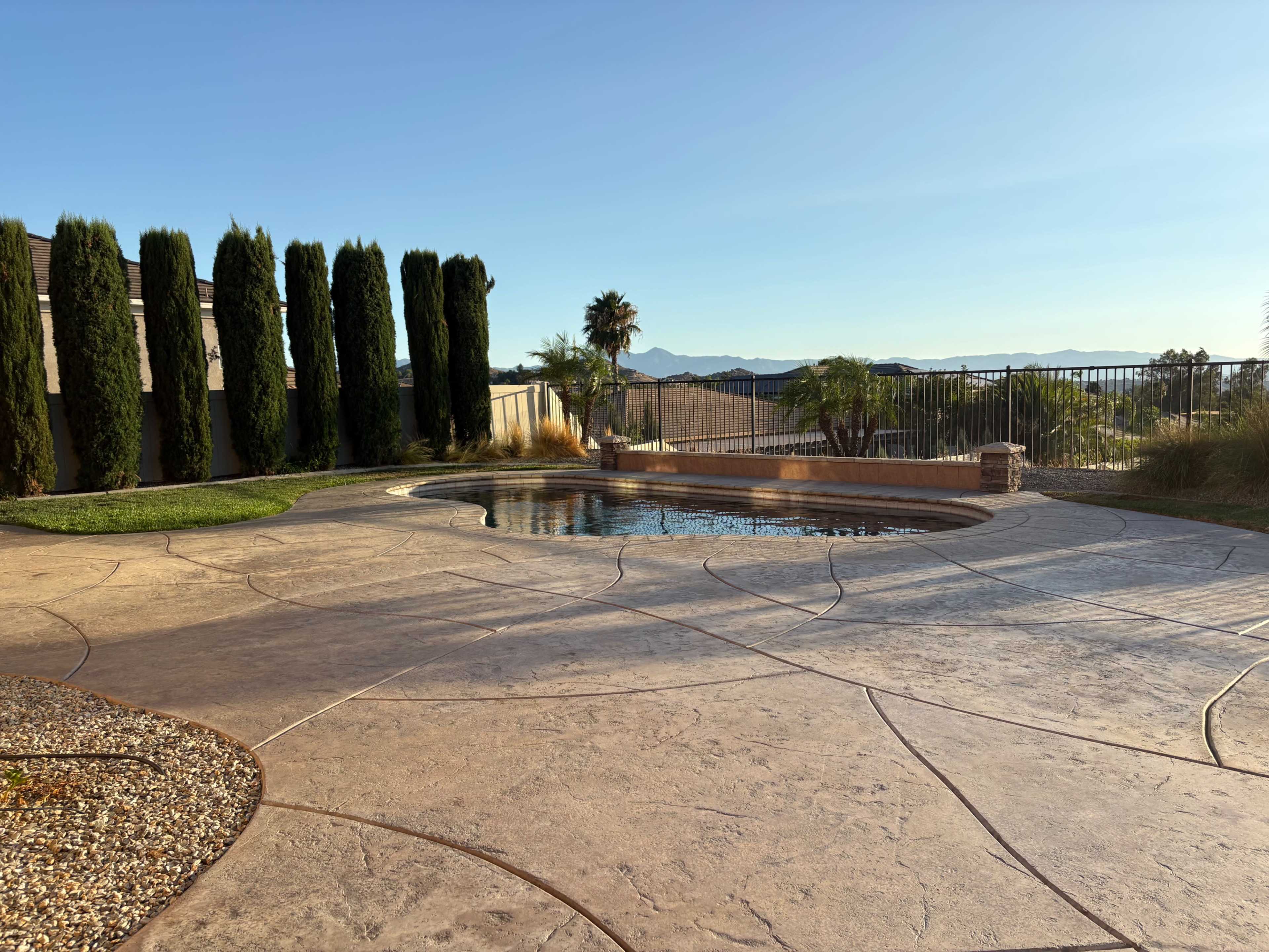 A curvilinear hot tub is positioned beside a polished concrete patio with a view of distant mountains and palm trees.
