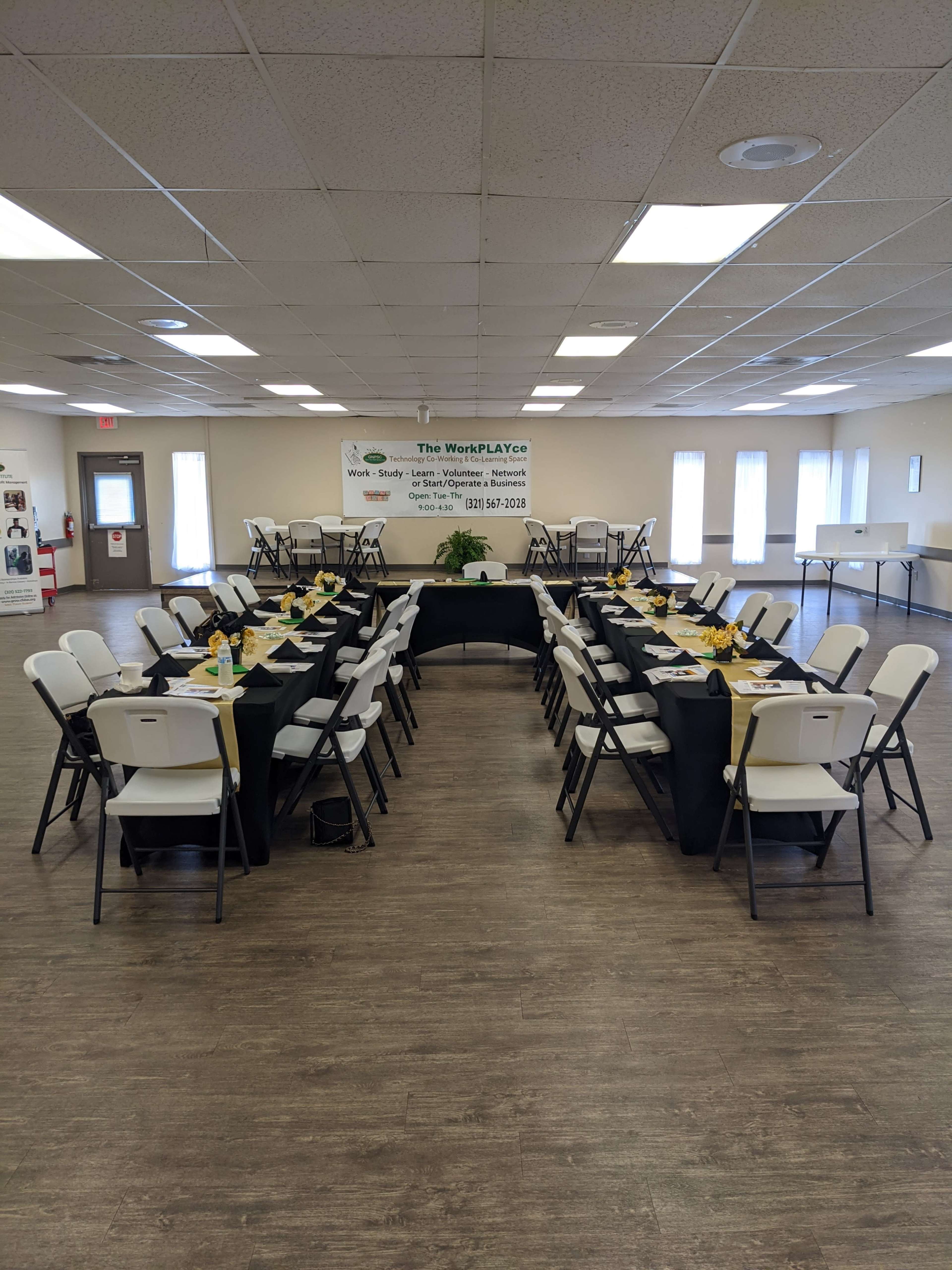 A set dining area is arranged with black tables and white chairs, featuring yellow napkins and a plant centerpiece in a well-lit room.