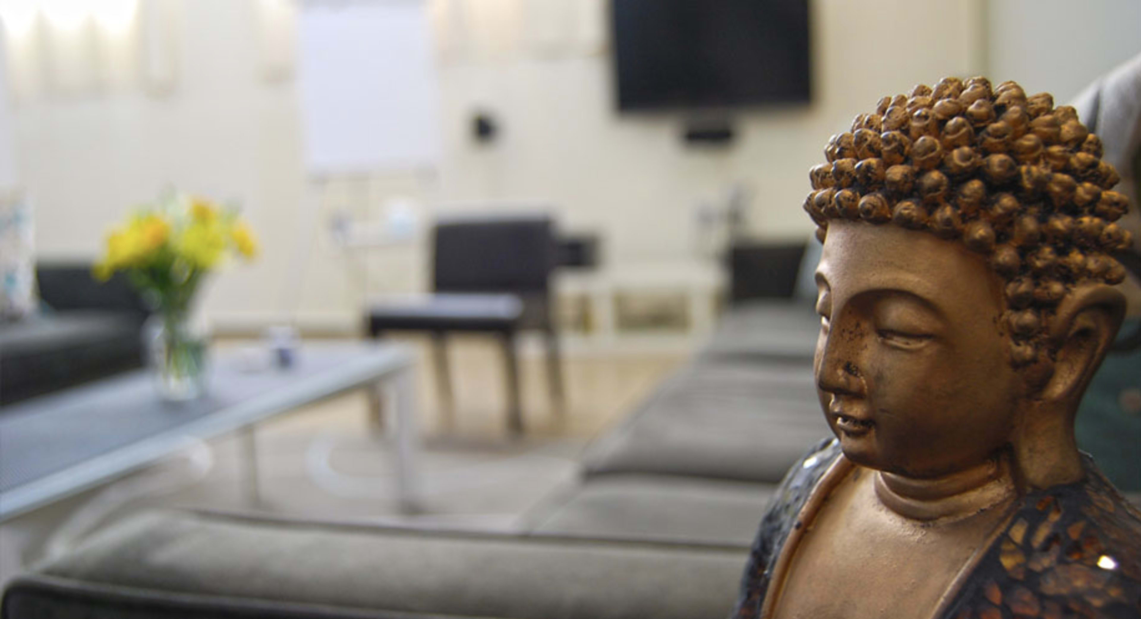 A Buddha statue is positioned in the foreground of a modern meeting room equipped with a television and seating.