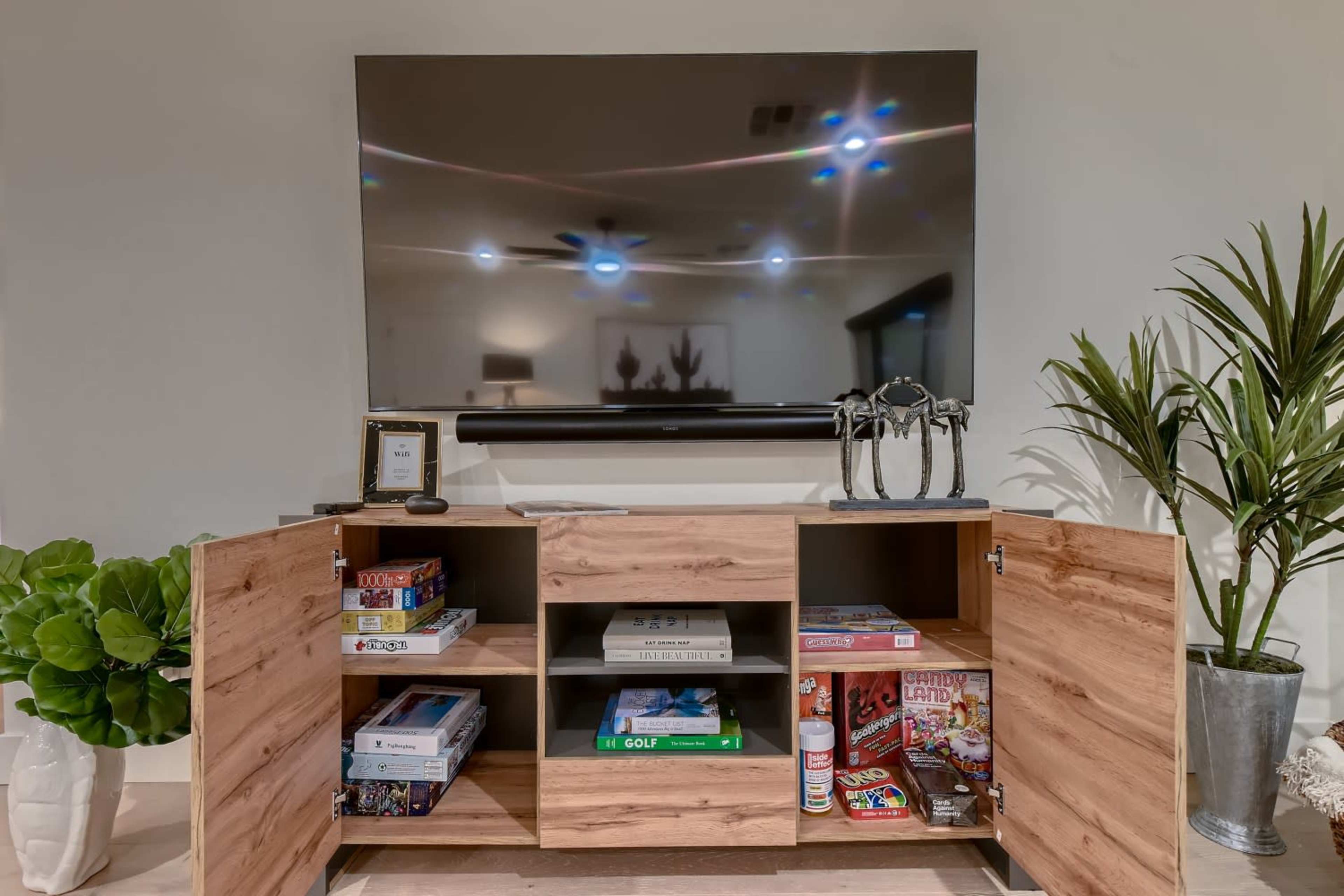 A wooden entertainment unit with an open design displays various board games and decorative items beneath a large flat-screen TV.