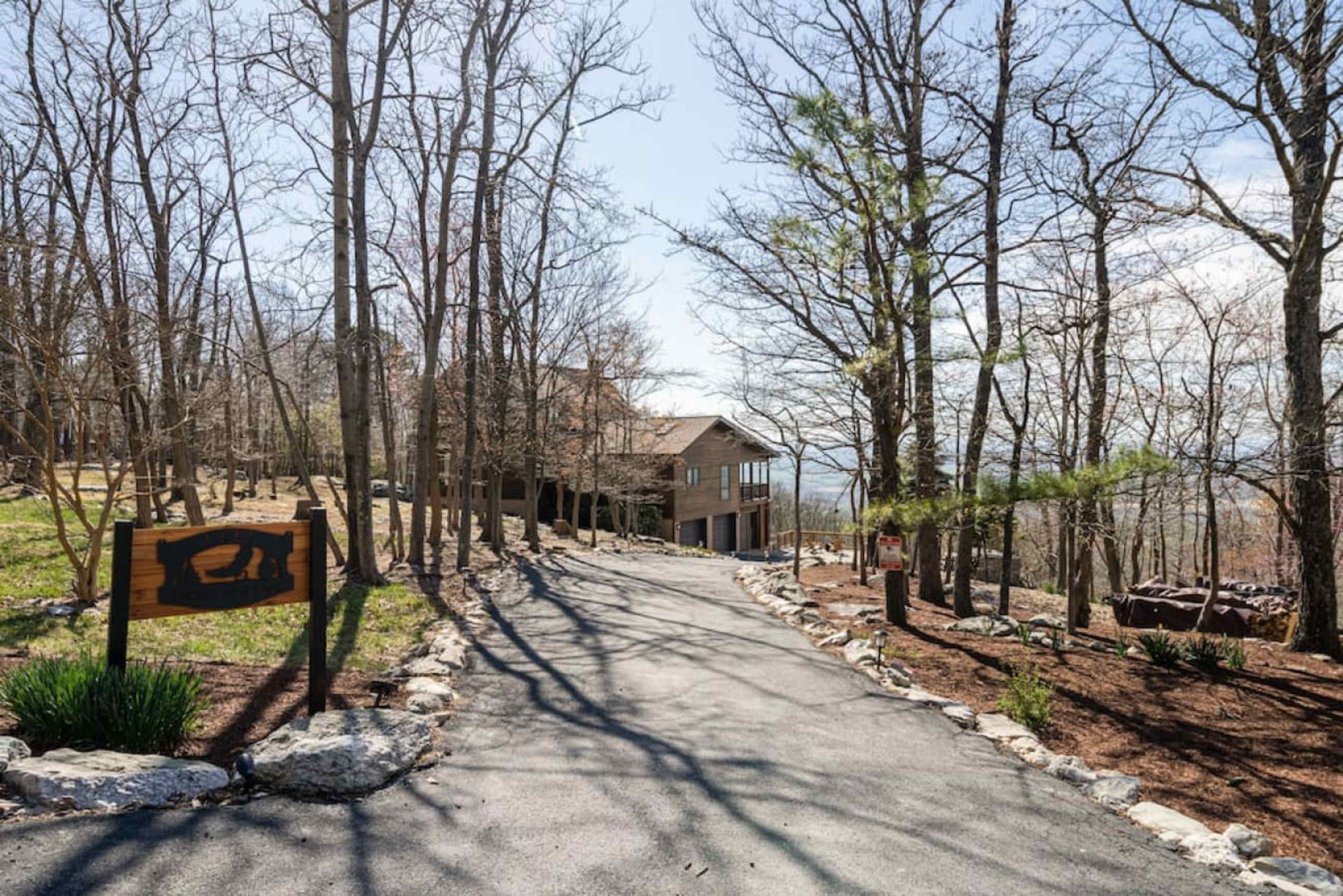 A gravel driveway leads to a wooden house surrounded by trees on a sunny day.