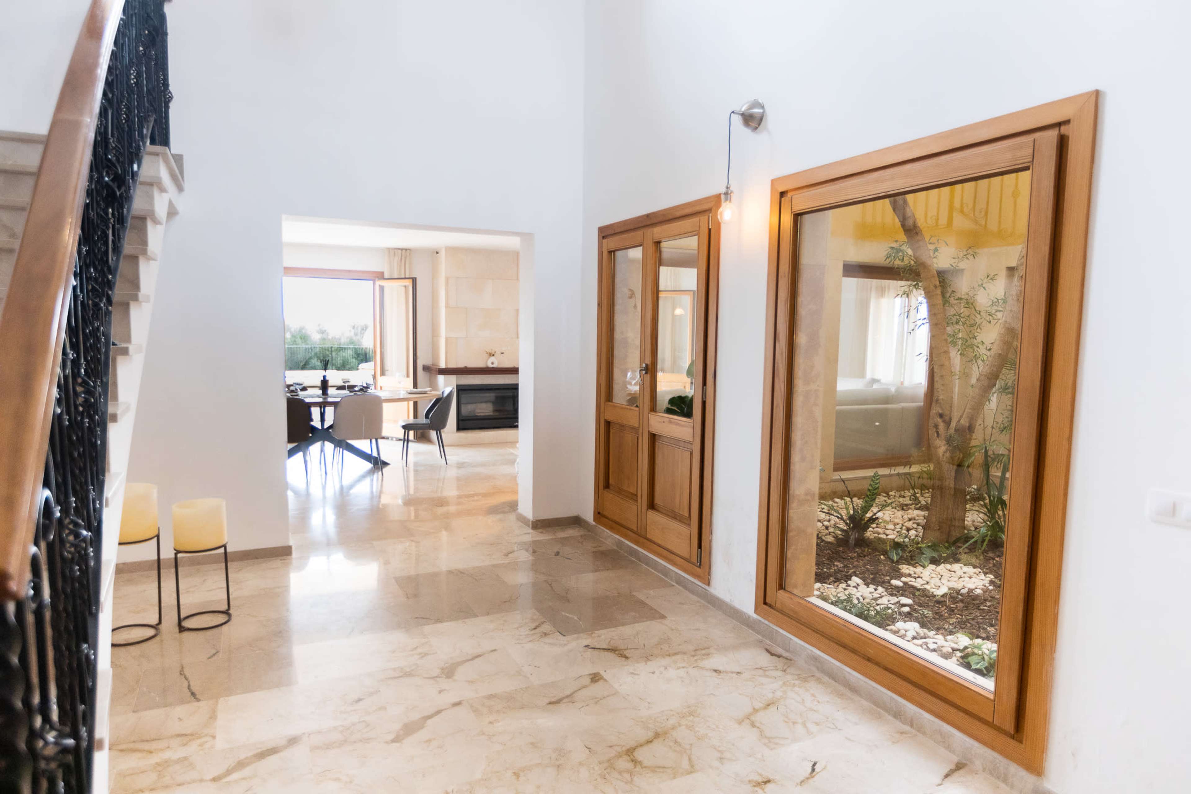 The image shows a spacious hallway with a staircase and large windows that look into a small indoor garden area.