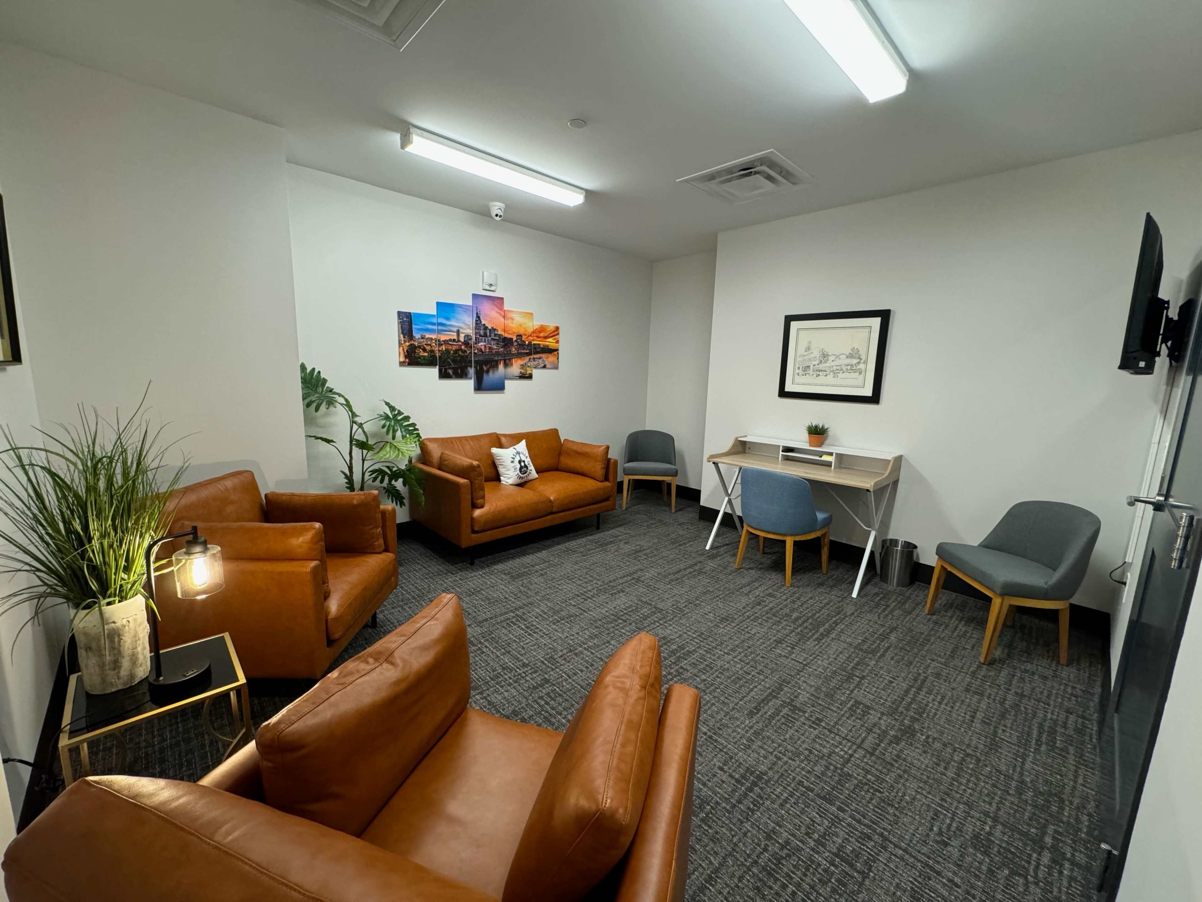 A modern interior lounge with brown leather chairs, a small desk, and decorative wall art in a well-lit room.