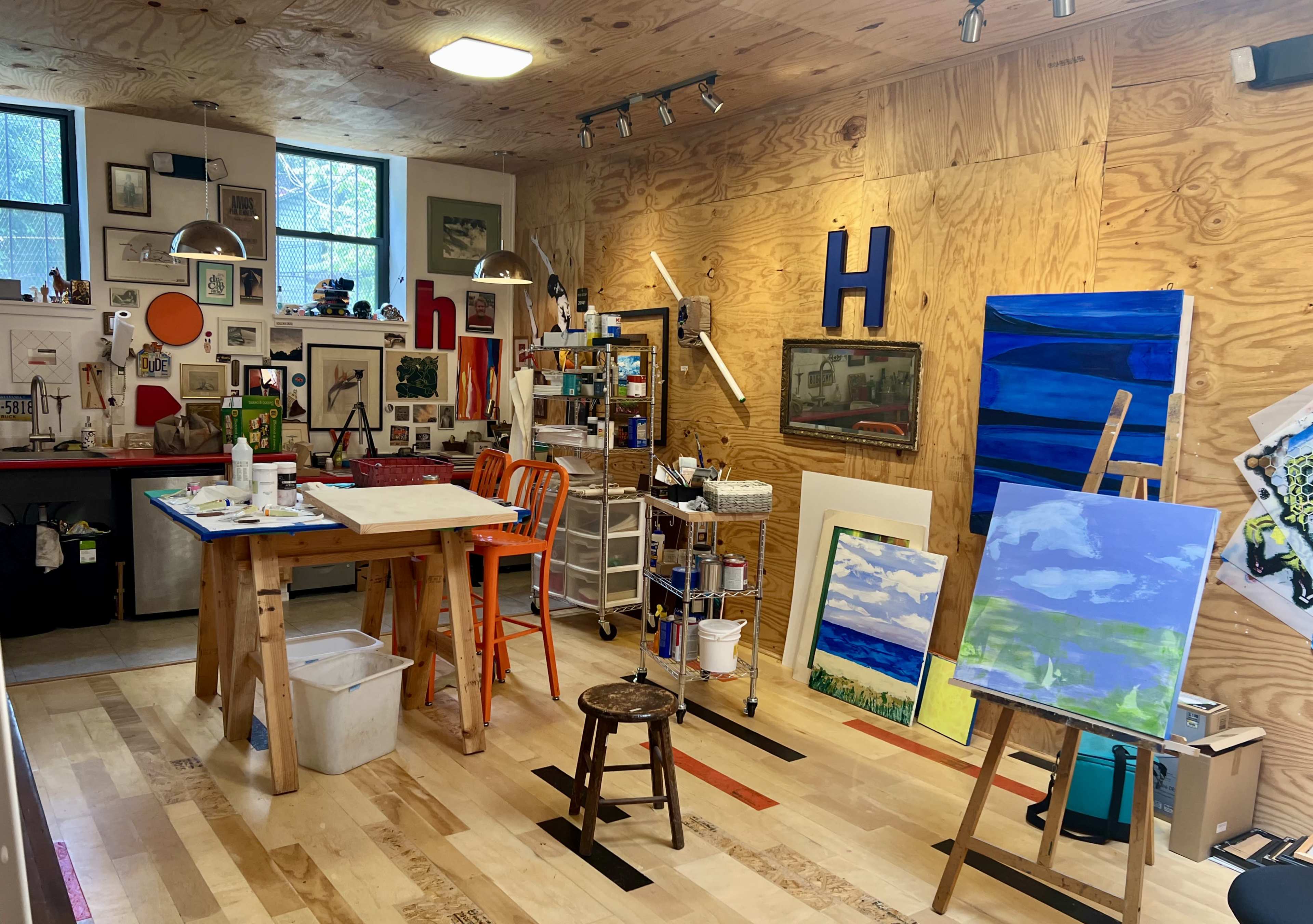 An artist's studio with wooden walls, various paintings on display, and an easel set up with art supplies.