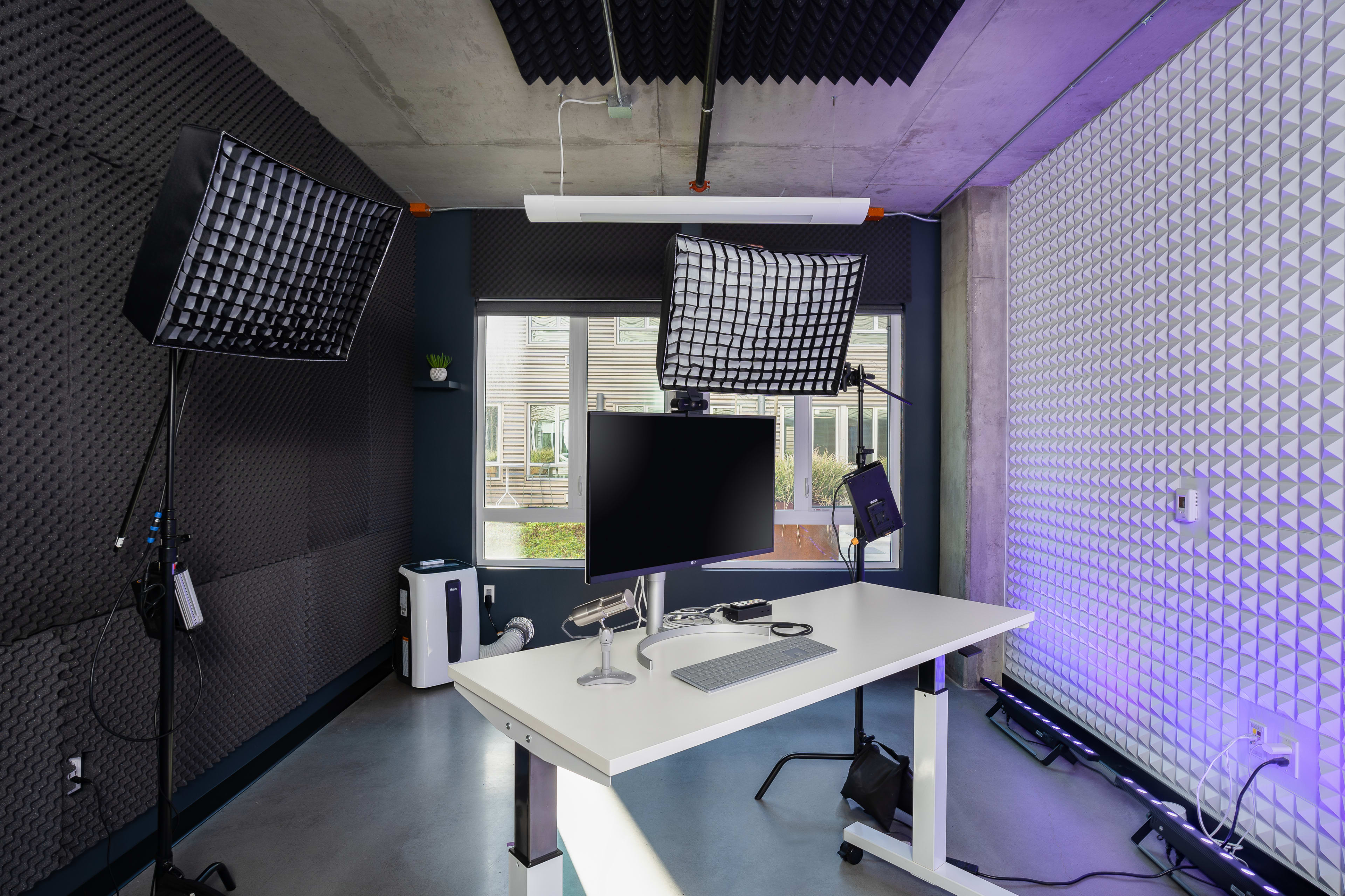 A modern office setup featuring a white desk with a monitor and keyboard, surrounded by sound-absorbing panels and studio lights.