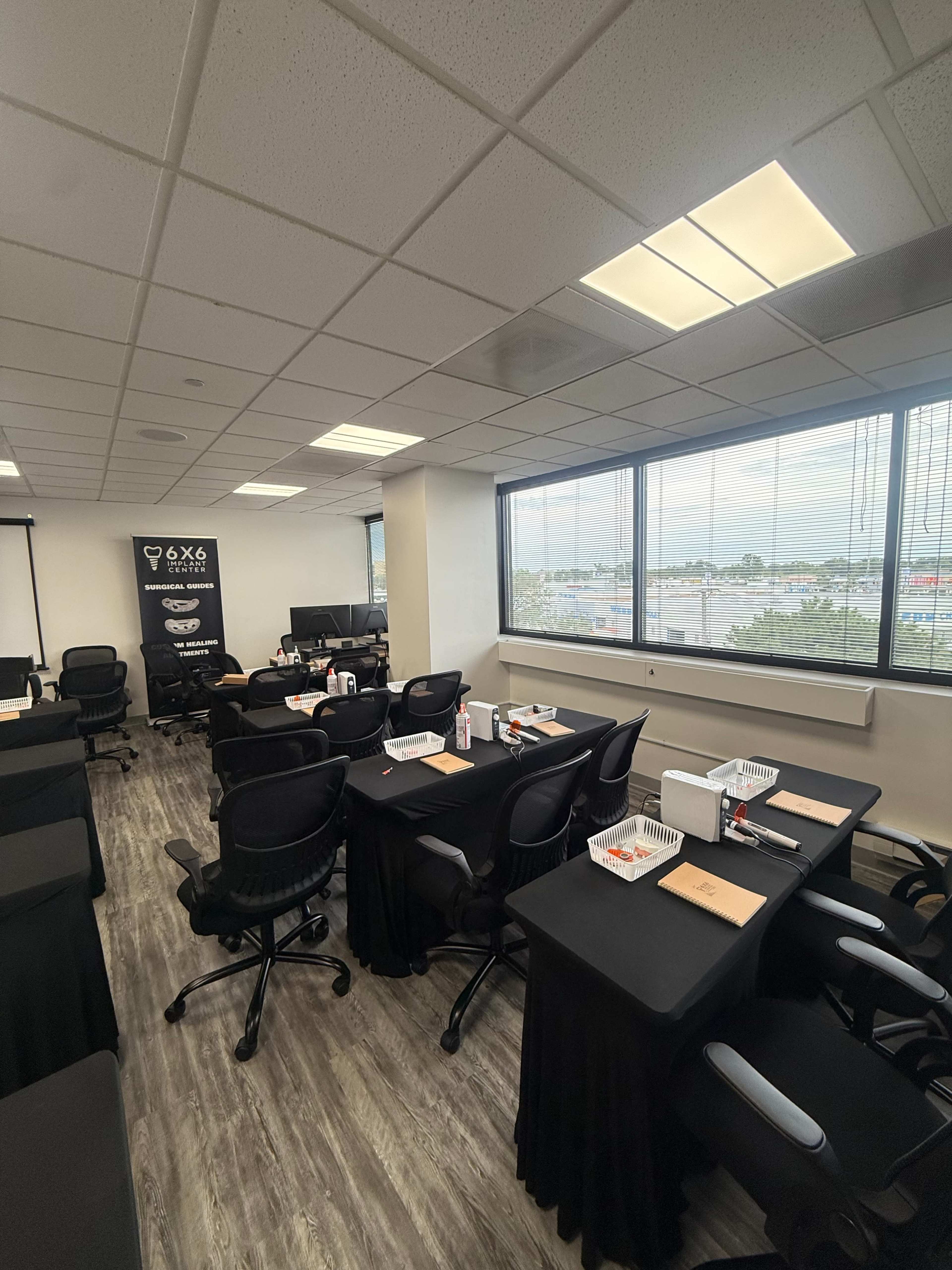 The image shows a conference room with several tables covered in black cloth and equipped with chairs, each prepared with materials for a seminar or presentation.