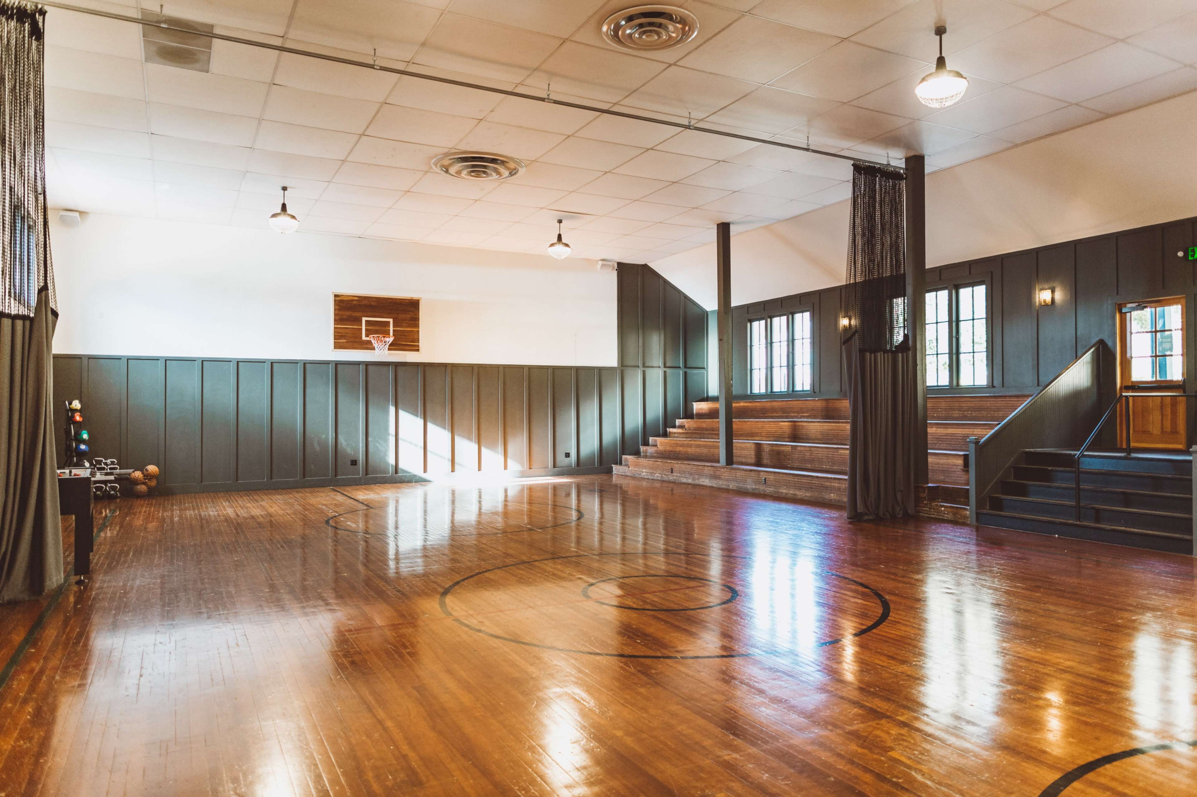 The image shows a spacious, well-lit indoor basketball court with wooden floors and tiered seating on one side.