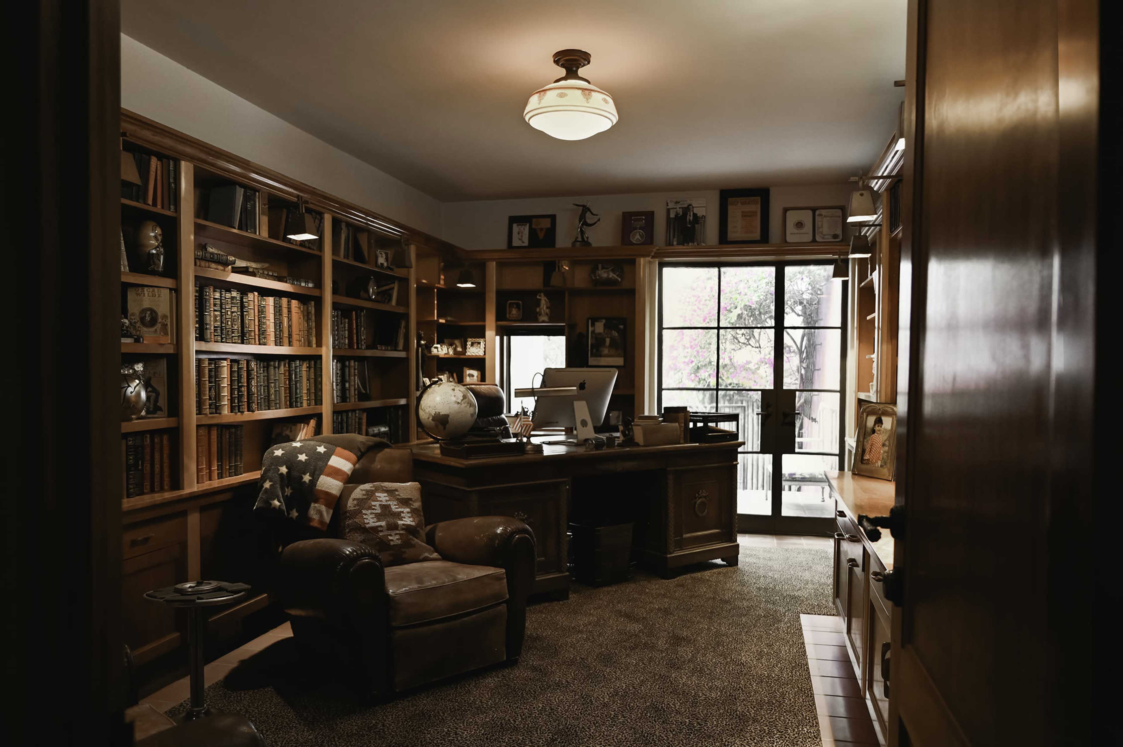 A home office featuring a wooden desk, a globe, bookshelves filled with books, and a seating area with a leather armchair.