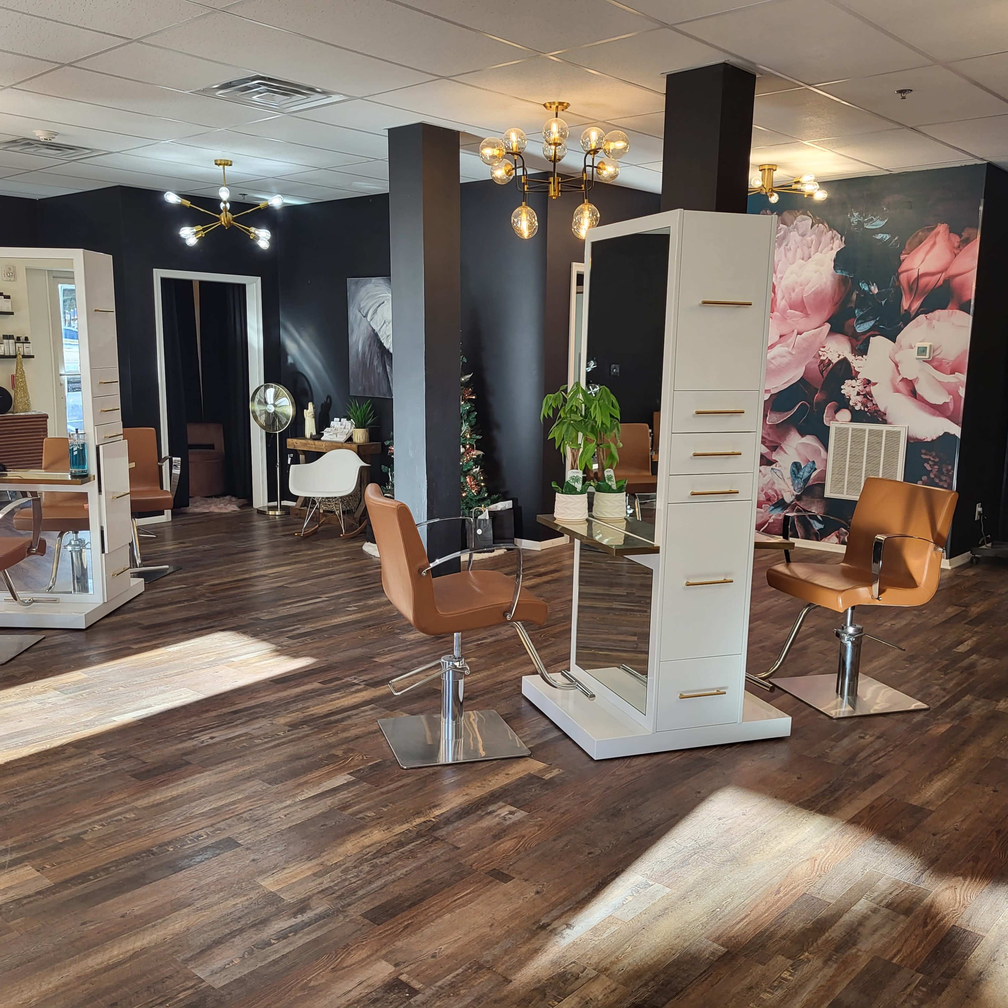 A modern hair salon with several styling stations, a decorative plant, and a floral mural on one wall.