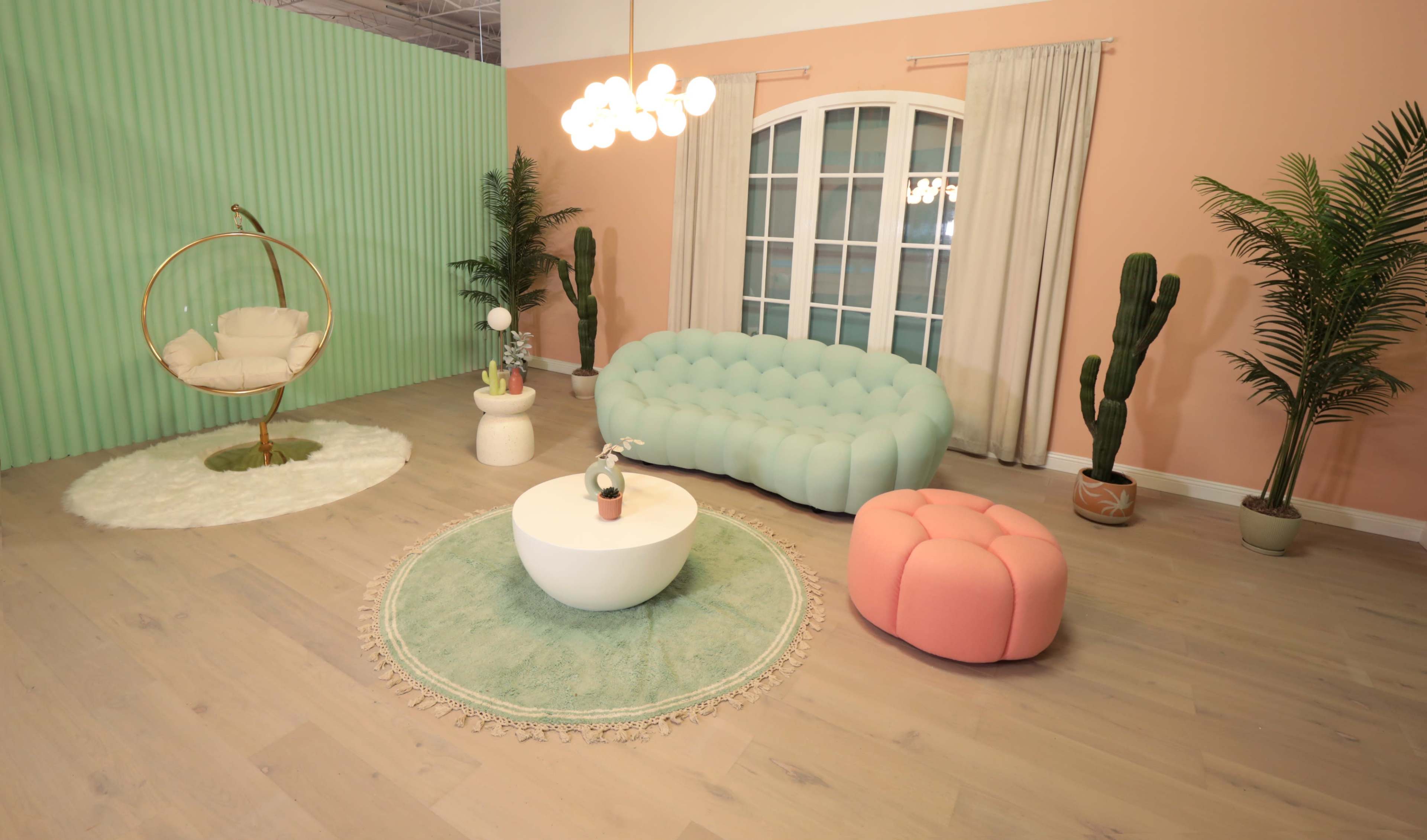 The scene features a modern, brightly colored living space with a mint green wall, a light blue sofa, a pink ottoman, a white coffee table, and decorative plants.