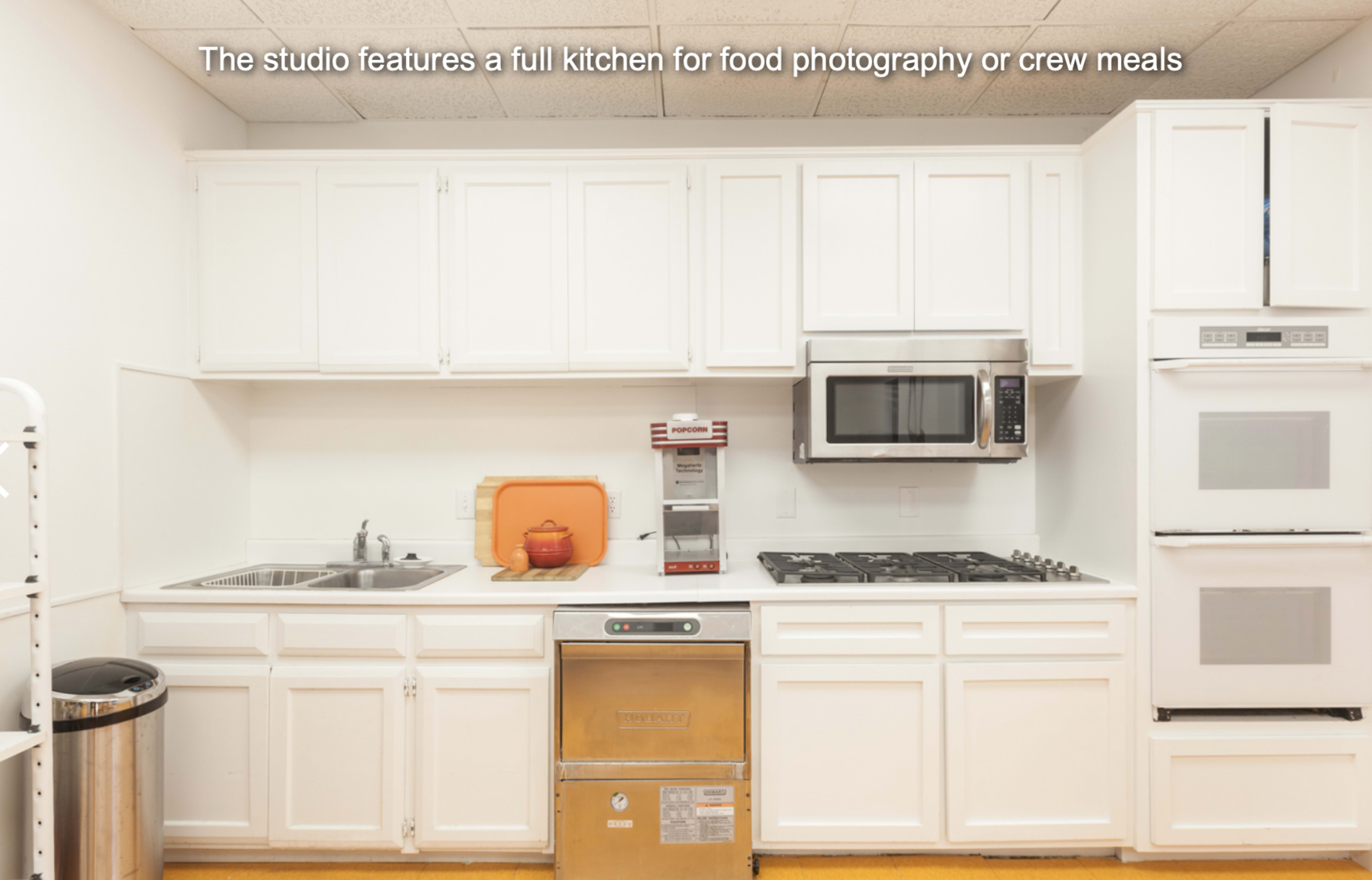 A white kitchen with a sink, microwave, oven, and stovetop, designed for food photography or crew meals.