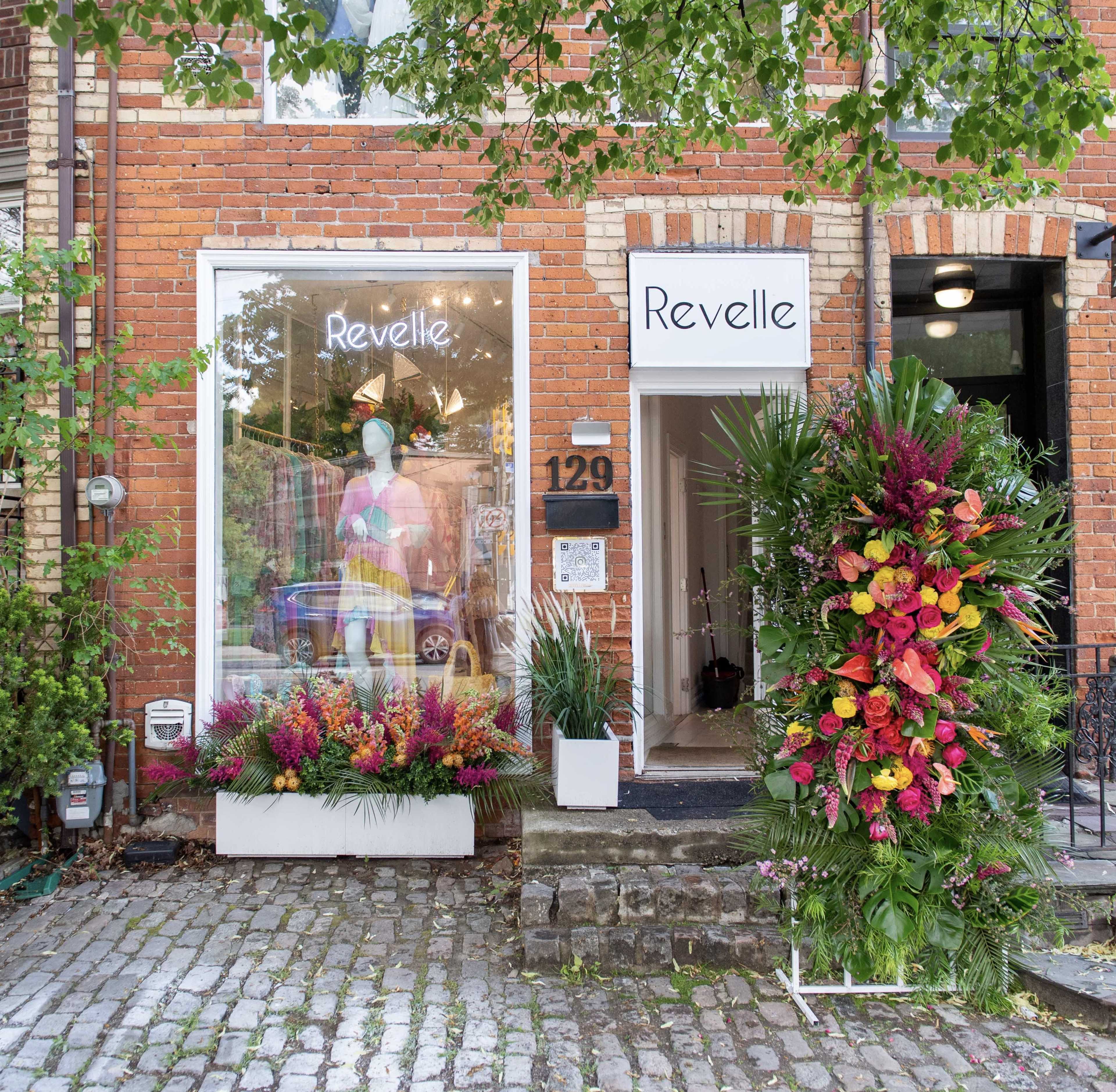 A boutique named "Revelle" features vibrant floral arrangements outside its brick facade, with a display mannequin in the window.