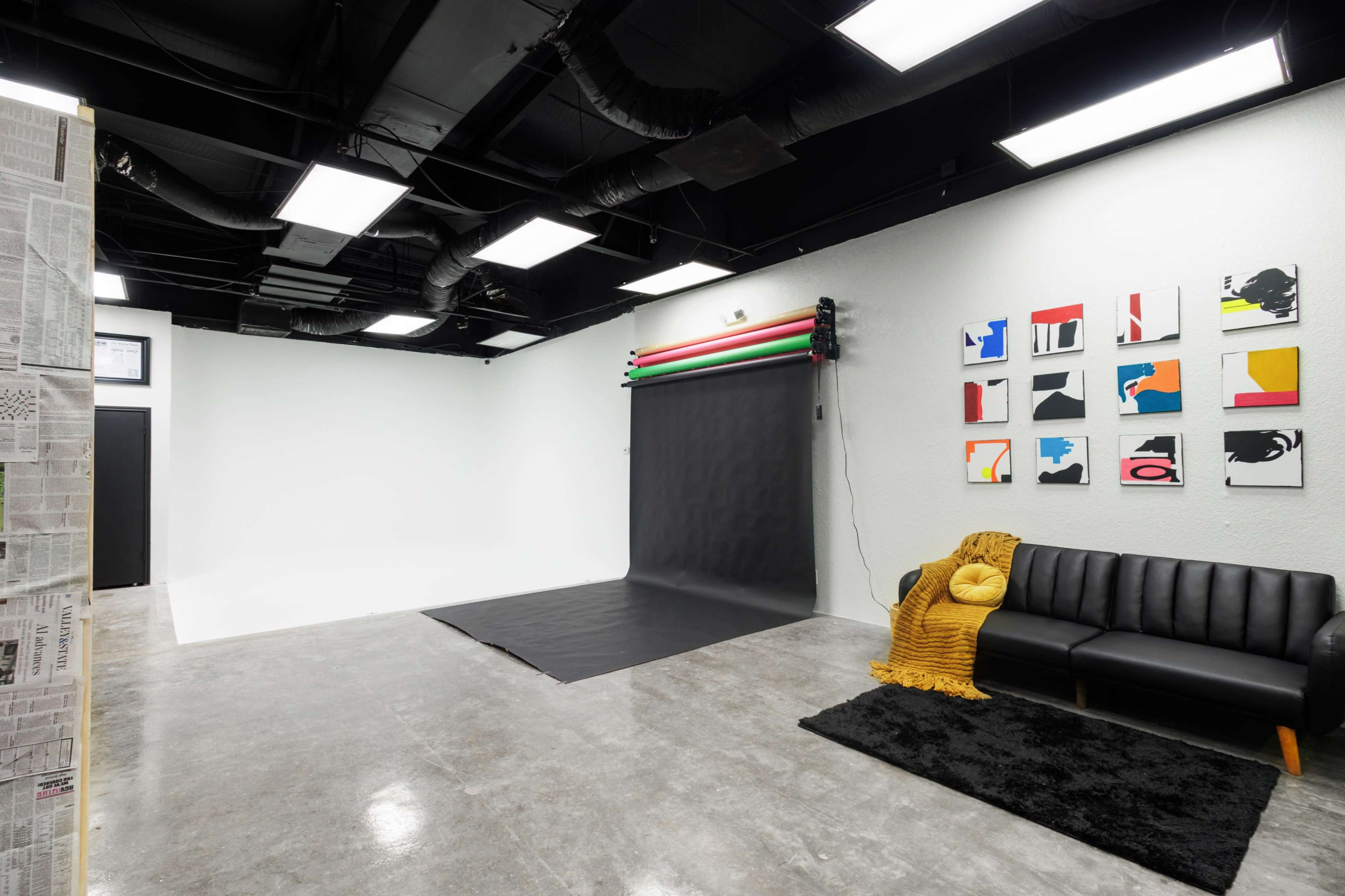 A photography studio featuring a black backdrop with colored lighting poles, a black sofa, and colorful artwork on the wall.