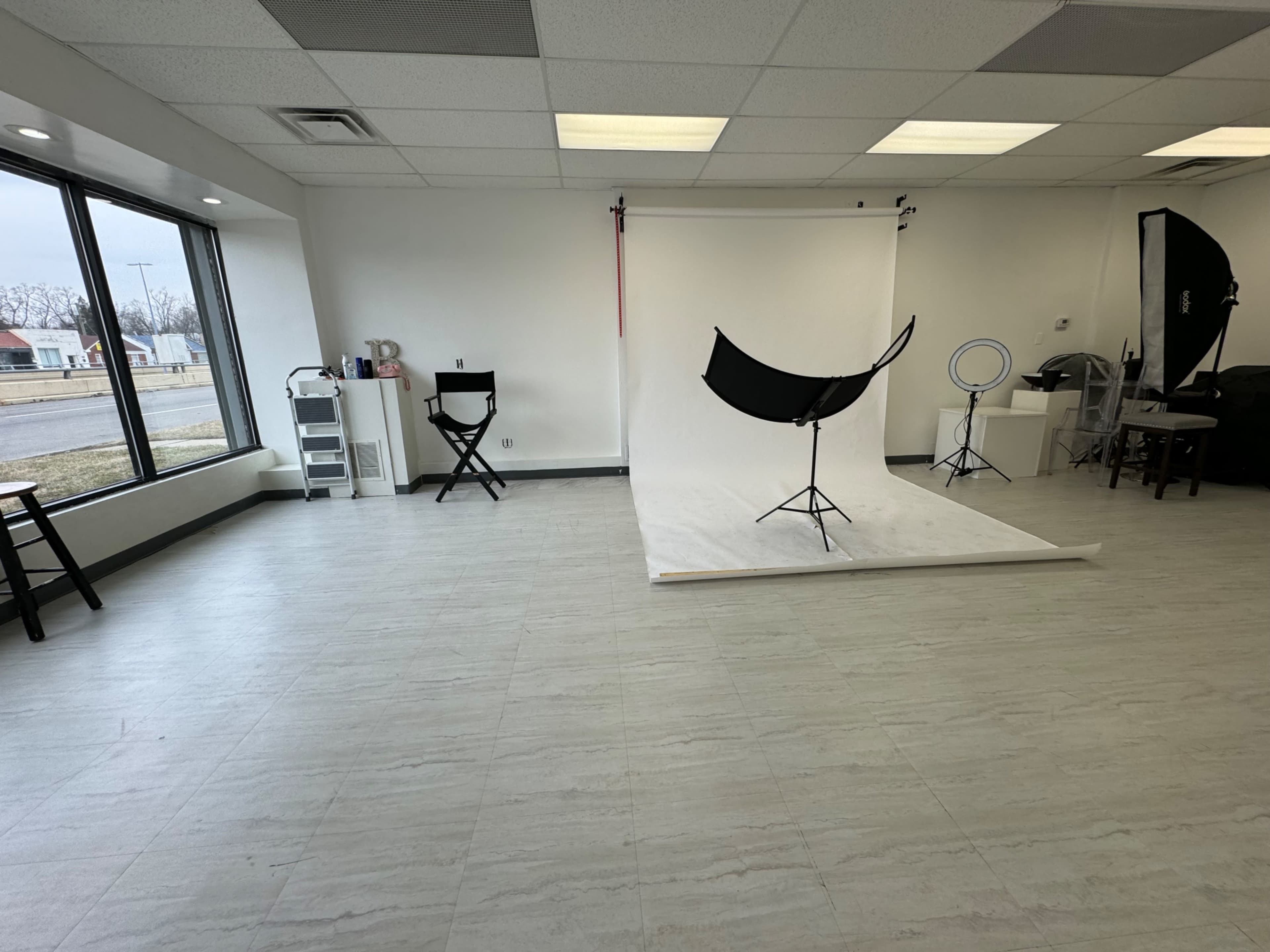 A photography studio with a white backdrop, multiple lighting setups, and empty seating areas.