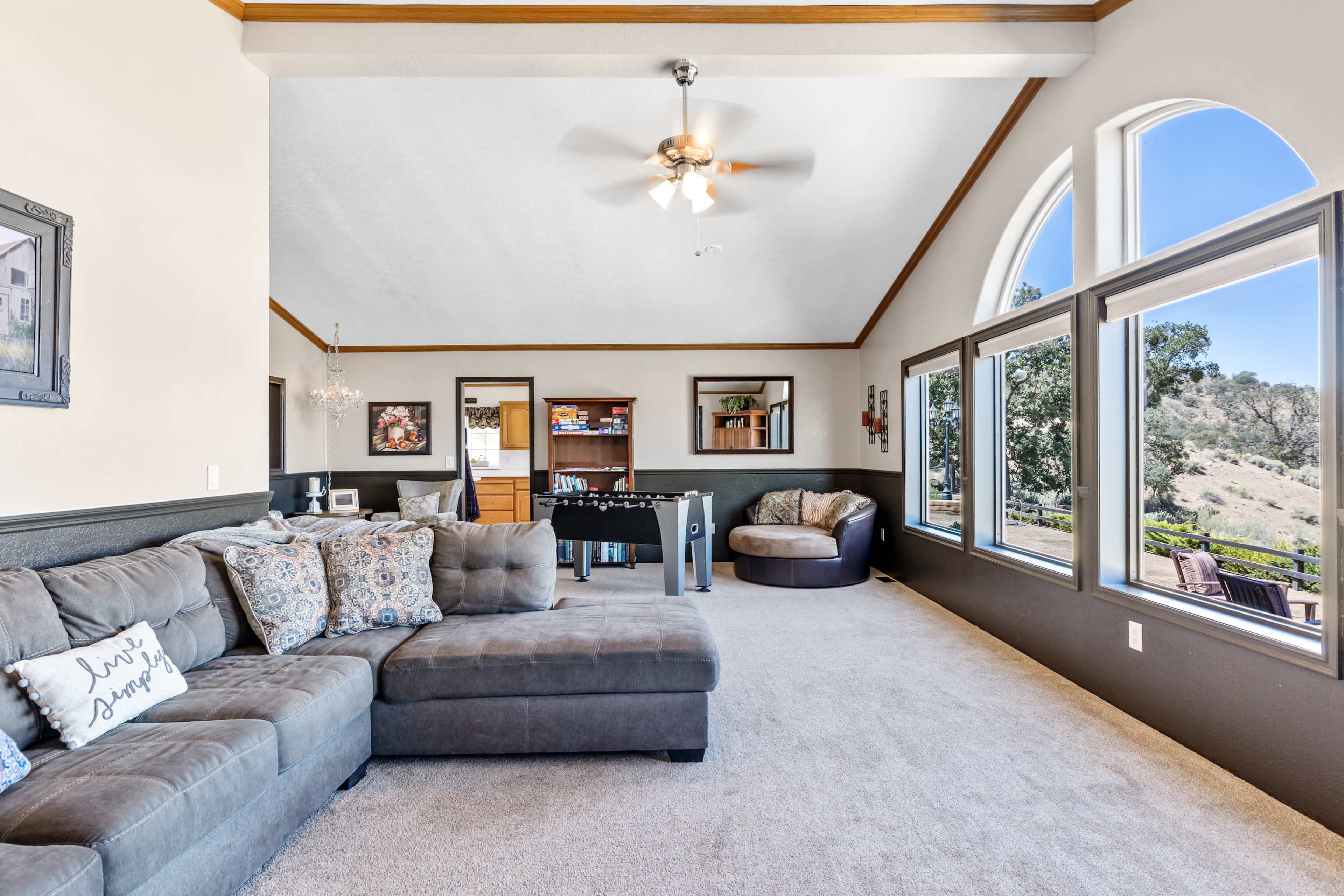A spacious living room features a sectional sofa, a pool table, and large windows with a view of the outdoors.