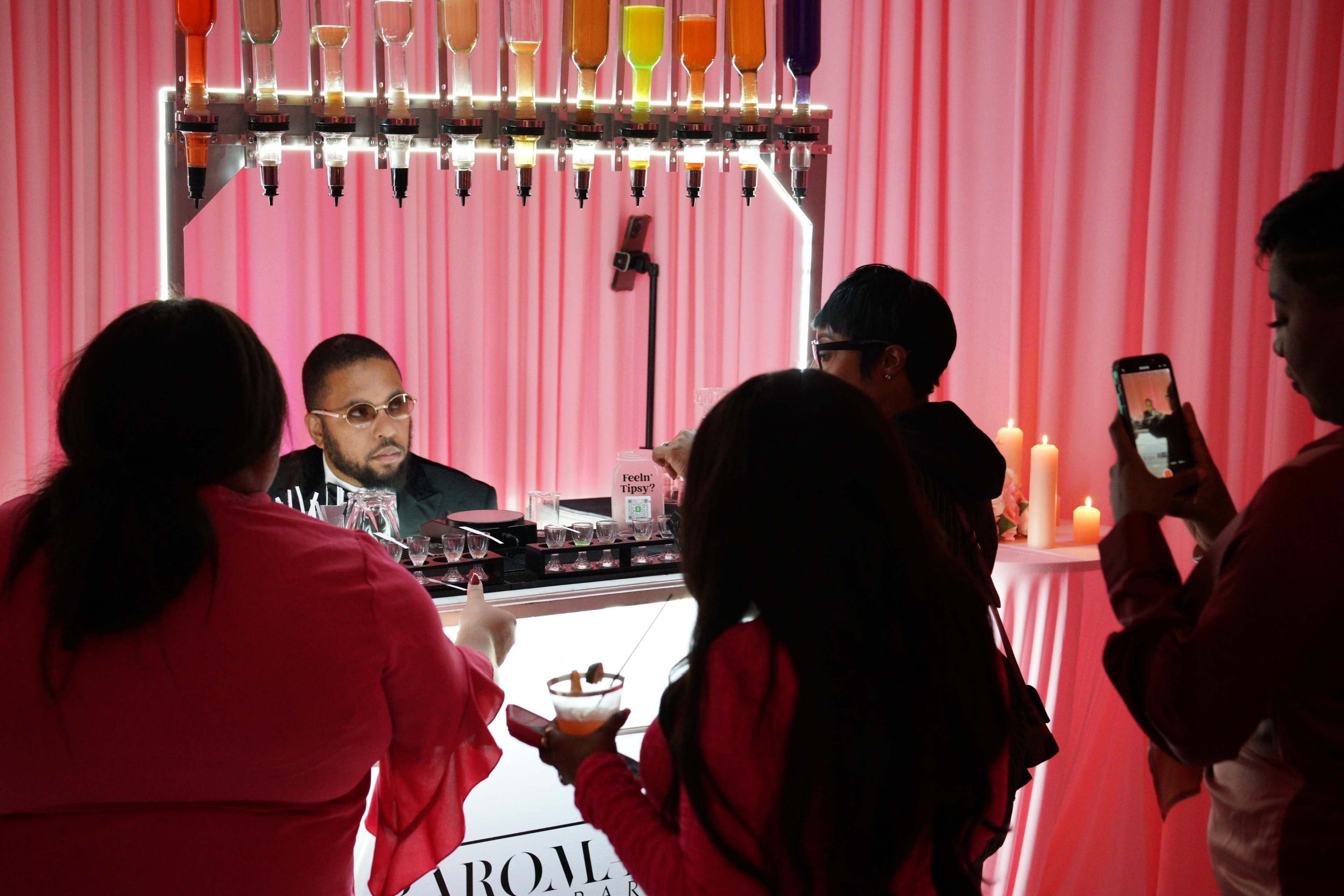 A bartender serves drinks to guests at a well-decorated bar with colorful mixers in a softly lit setting.