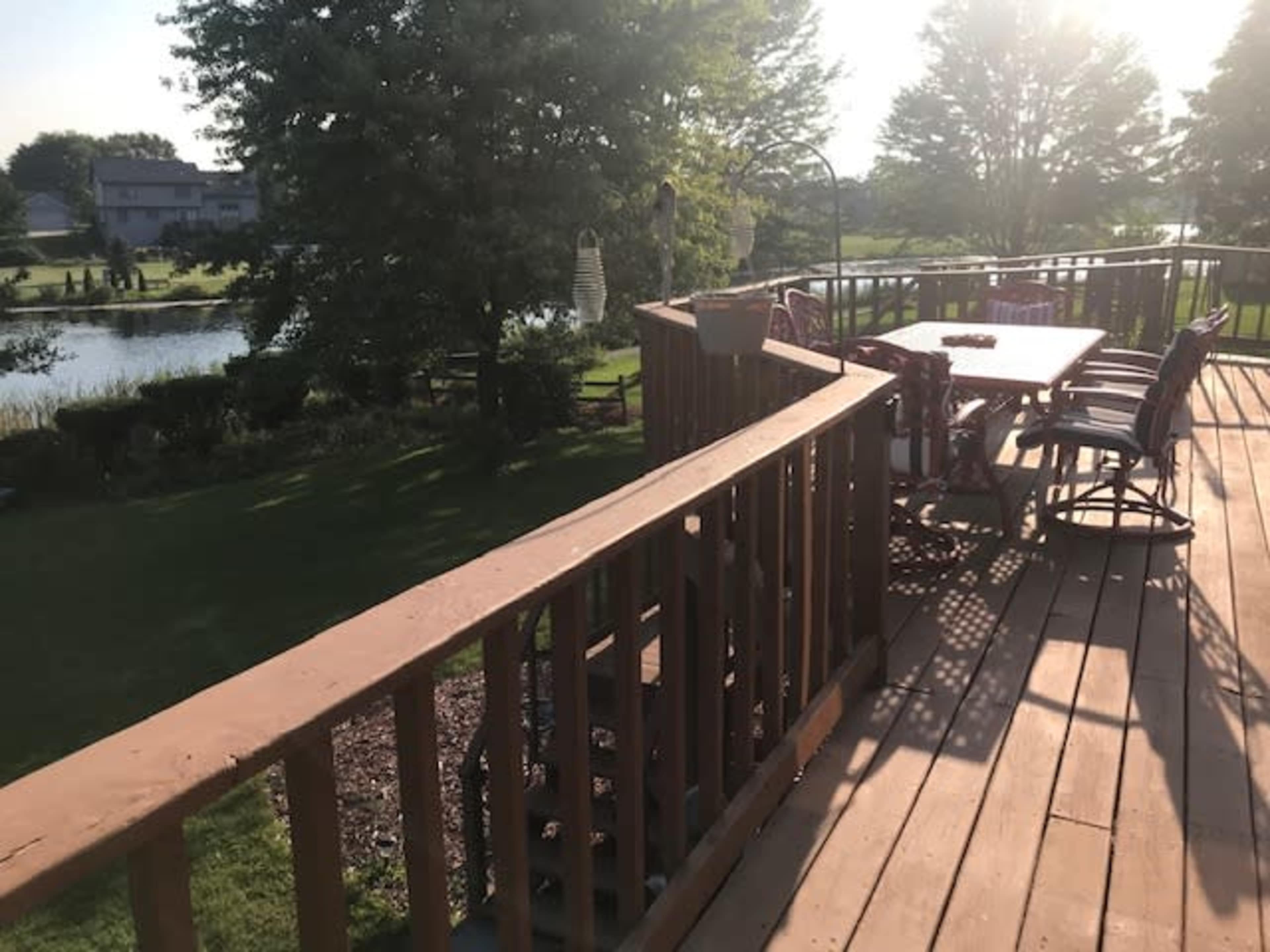A wooden deck with a table and chairs overlooks a pond surrounded by greenery.
