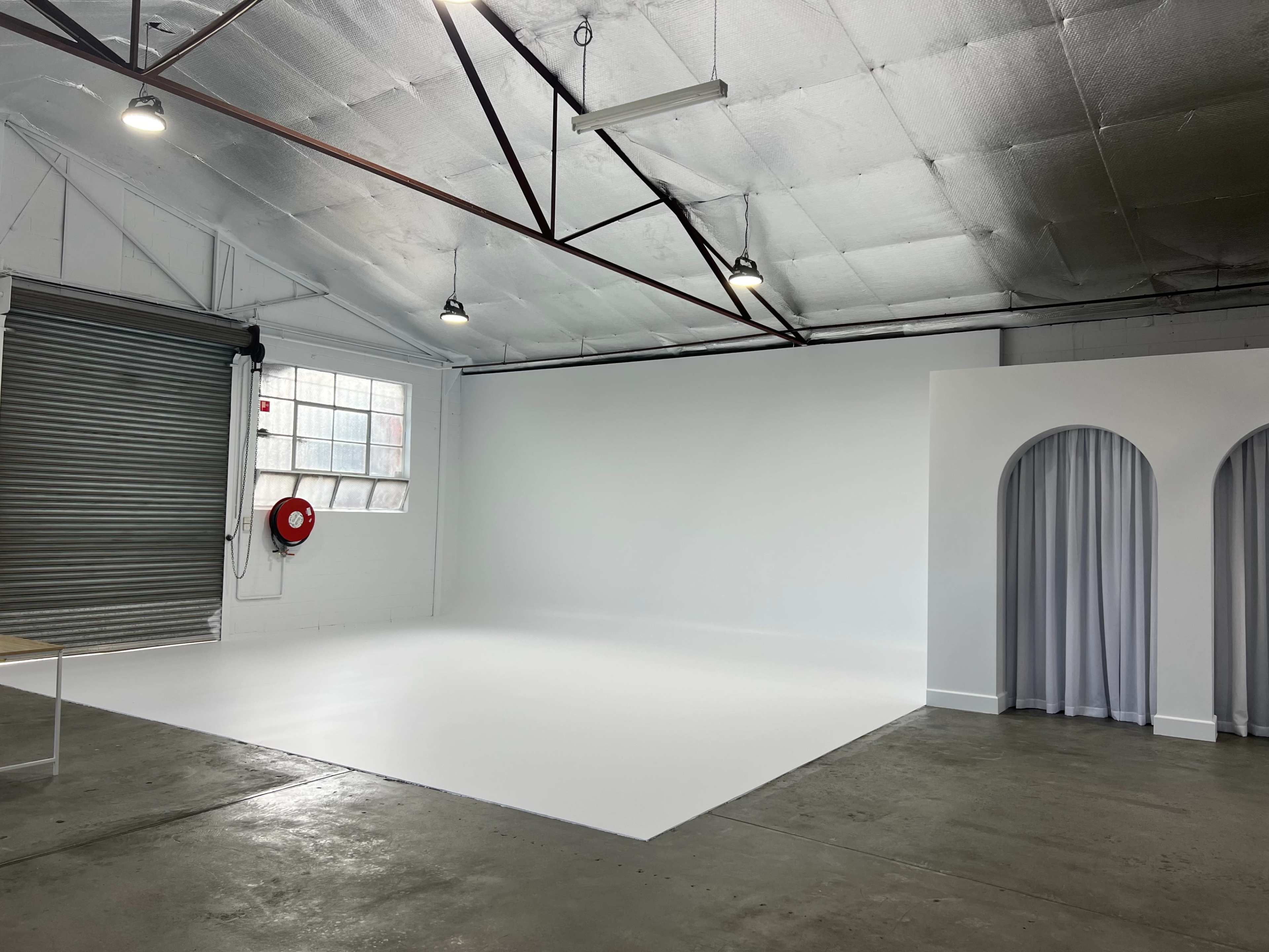 A spacious, well-lit studio with a white backdrop, large windows, and a gray curtain along one side.