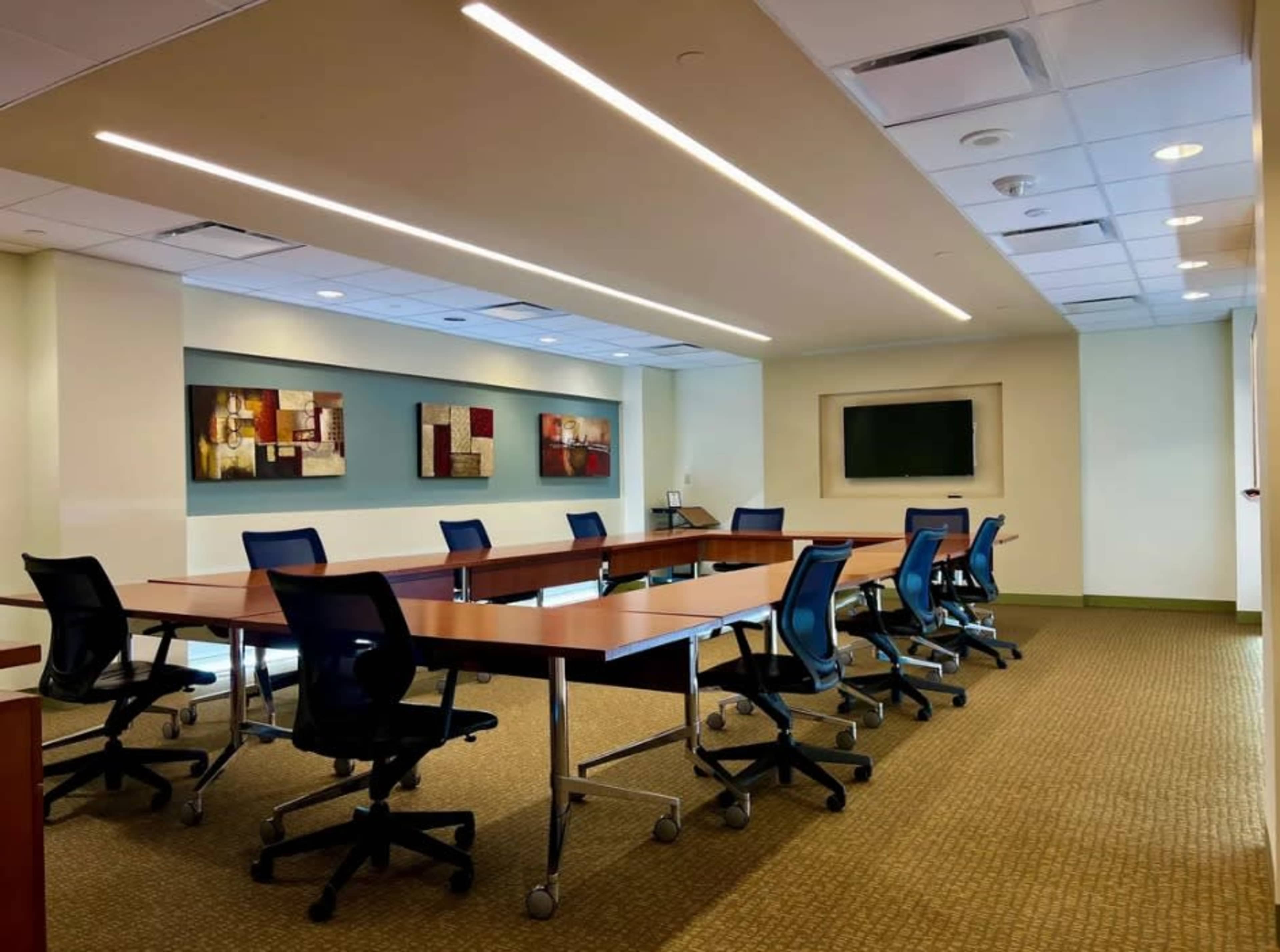 A modern conference room with a long table surrounded by rolling chairs, featuring artwork on the walls and a large screen for presentations.
