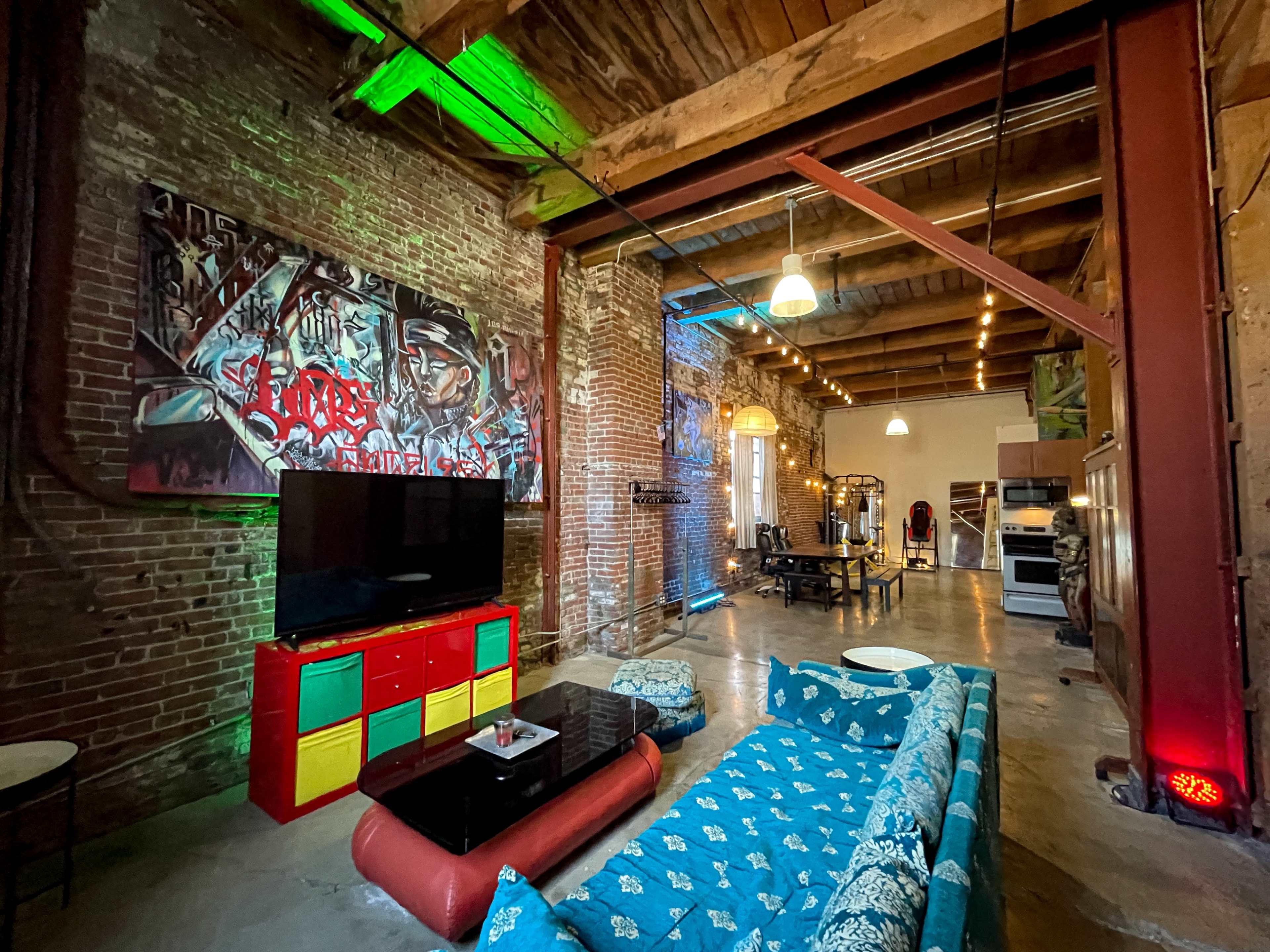A spacious loft with exposed brick walls, colorful furniture, and a large television in a modern living area.