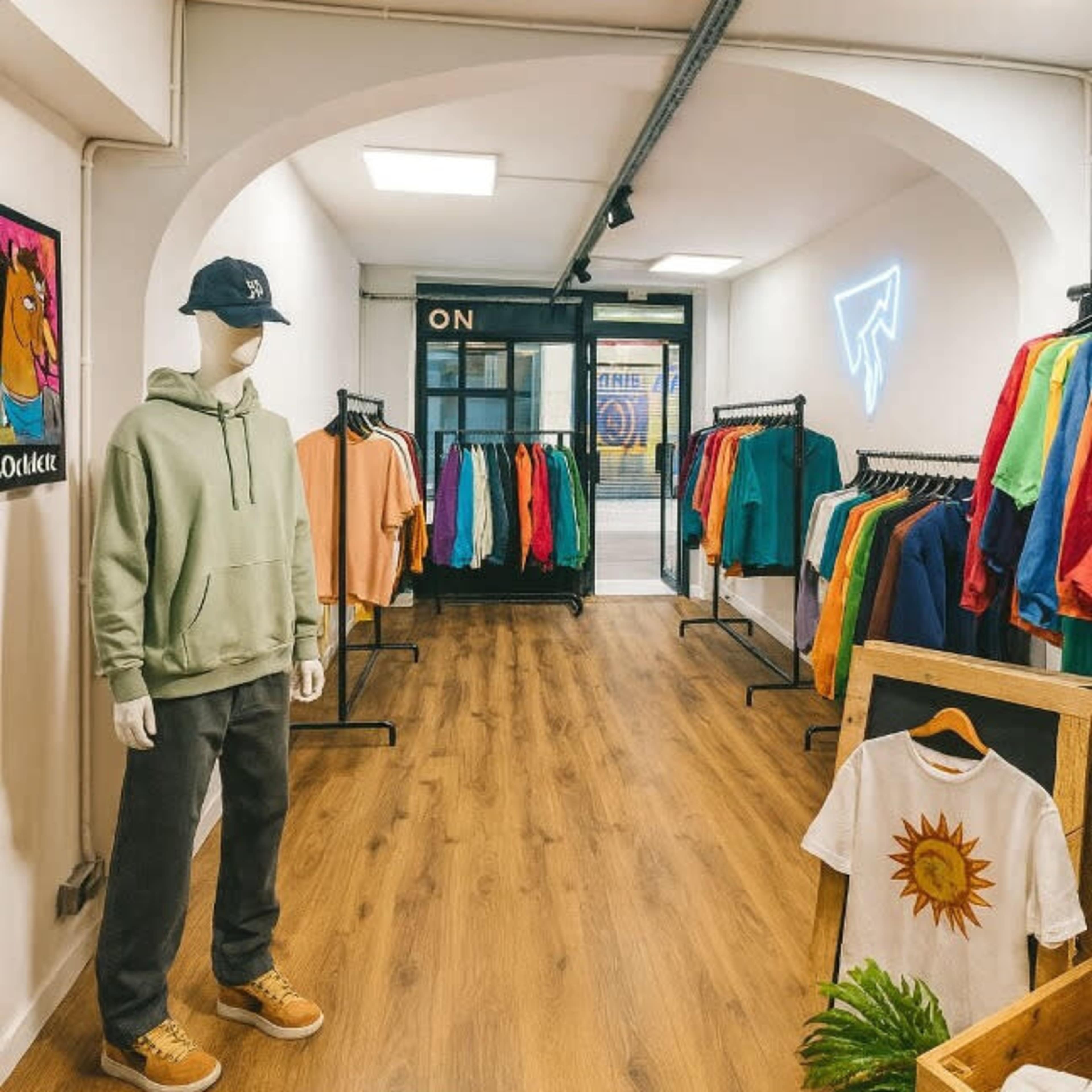 The image depicts a clothing store interior featuring a mannequin dressed in casual attire, with racks of colorful apparel lining the walls and wooden flooring.