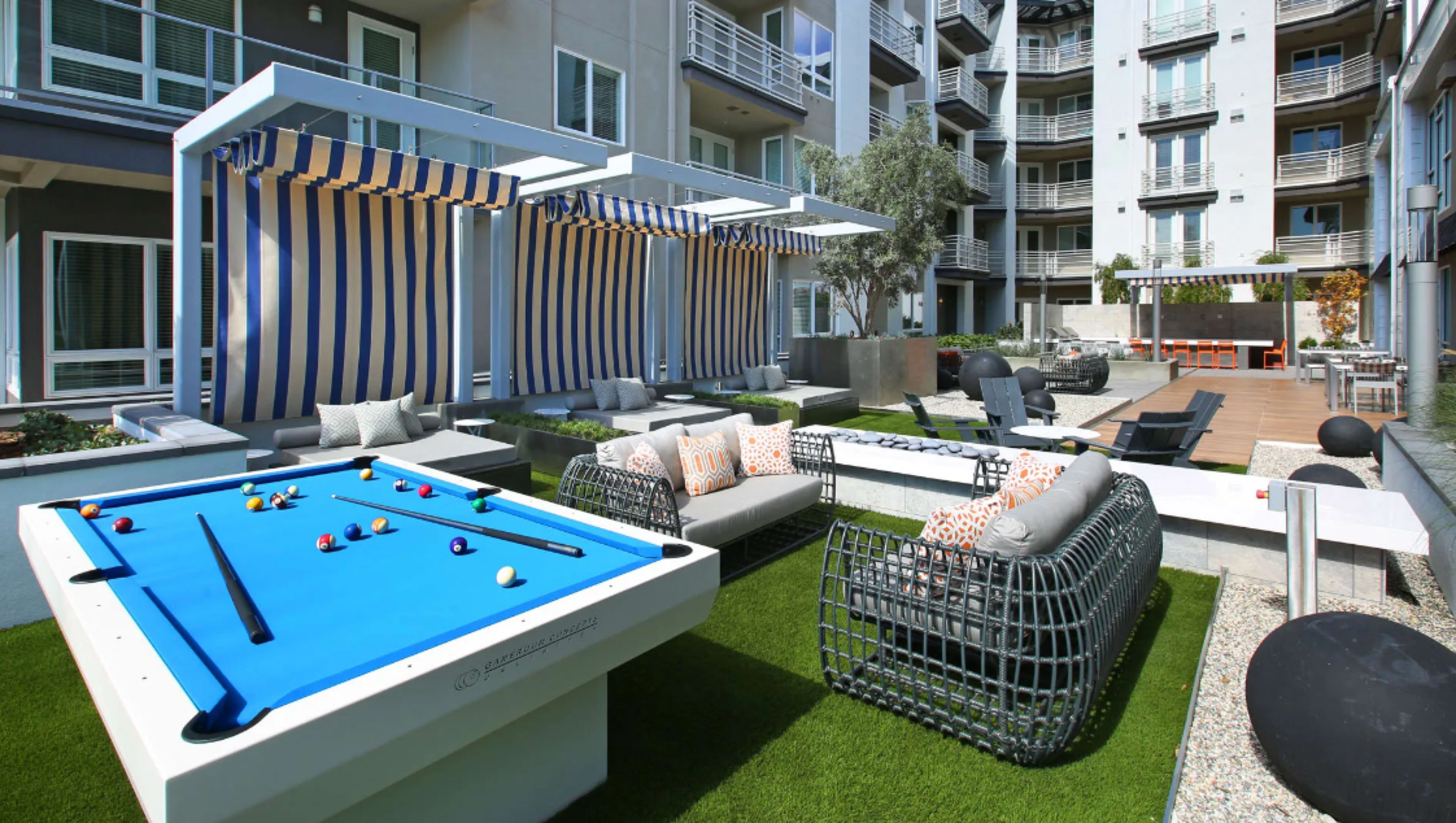 A modern outdoor lounge area featuring a pool table, lounge seating, and canopies.
