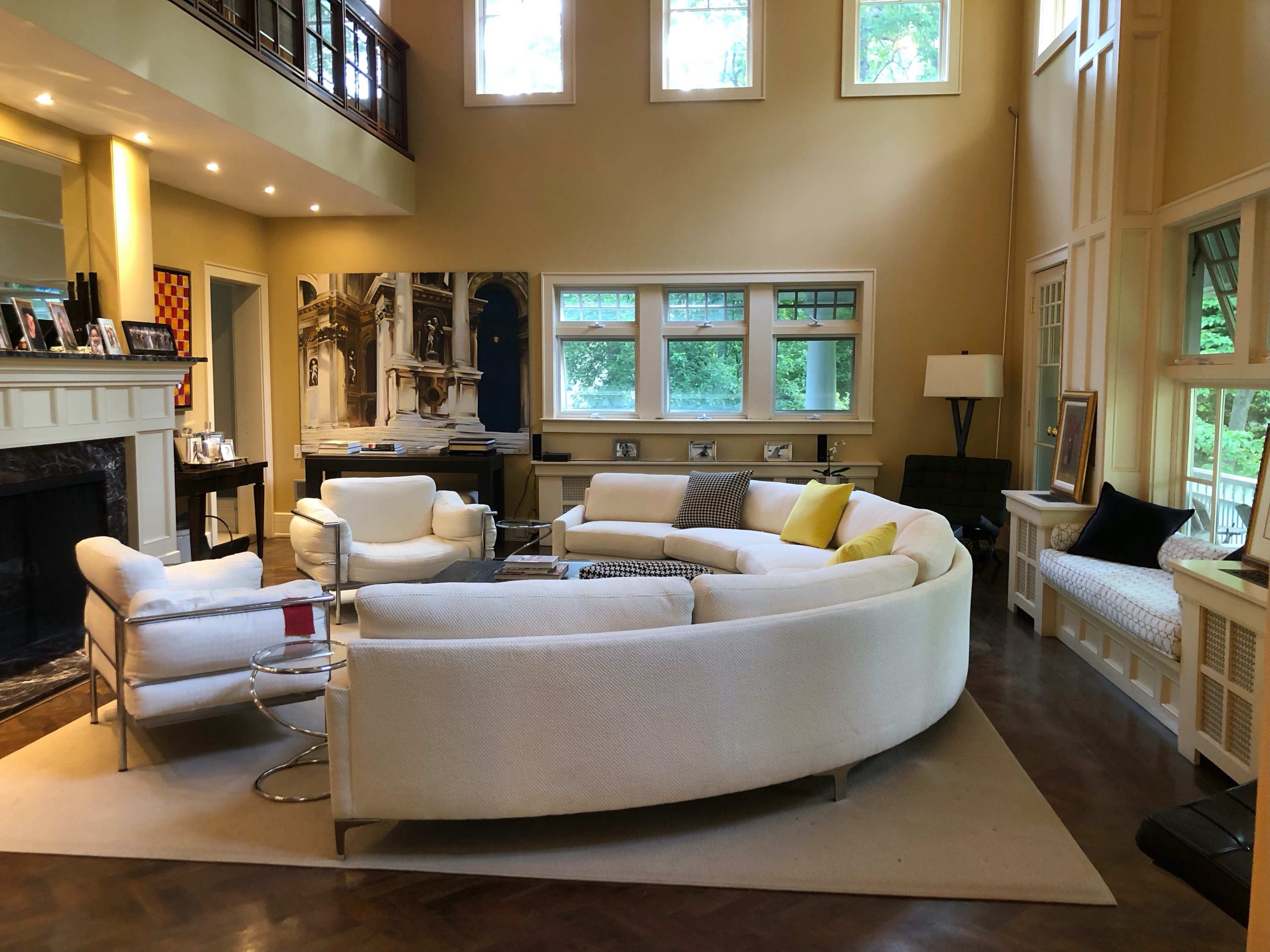 A spacious living room featuring a large, curved white sofa, two armchairs, and a coffee table, with large windows letting in natural light.