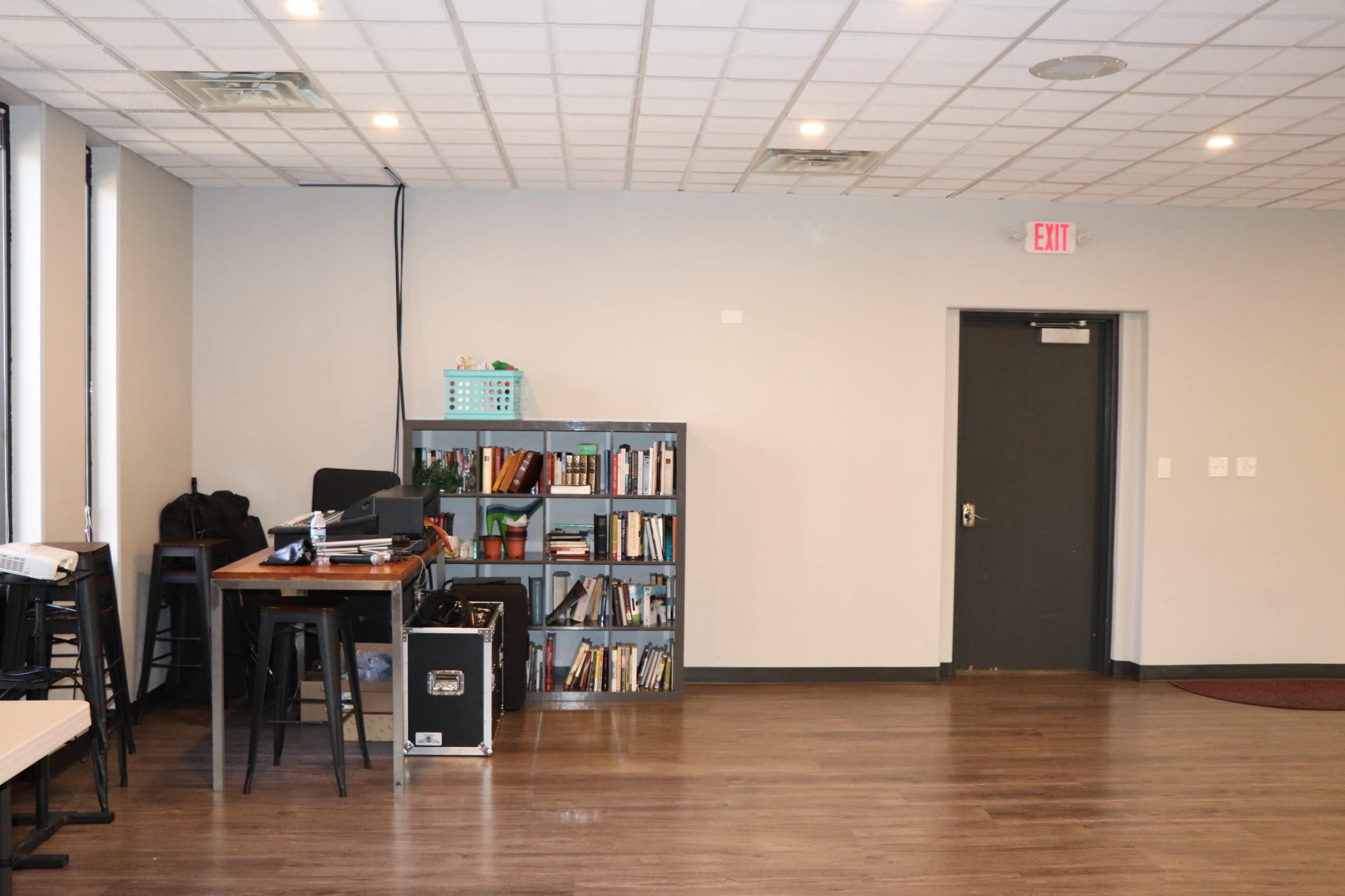 The image shows a room with a bookshelf, a small table, and a door, featuring hardwood floors and a drop ceiling.
