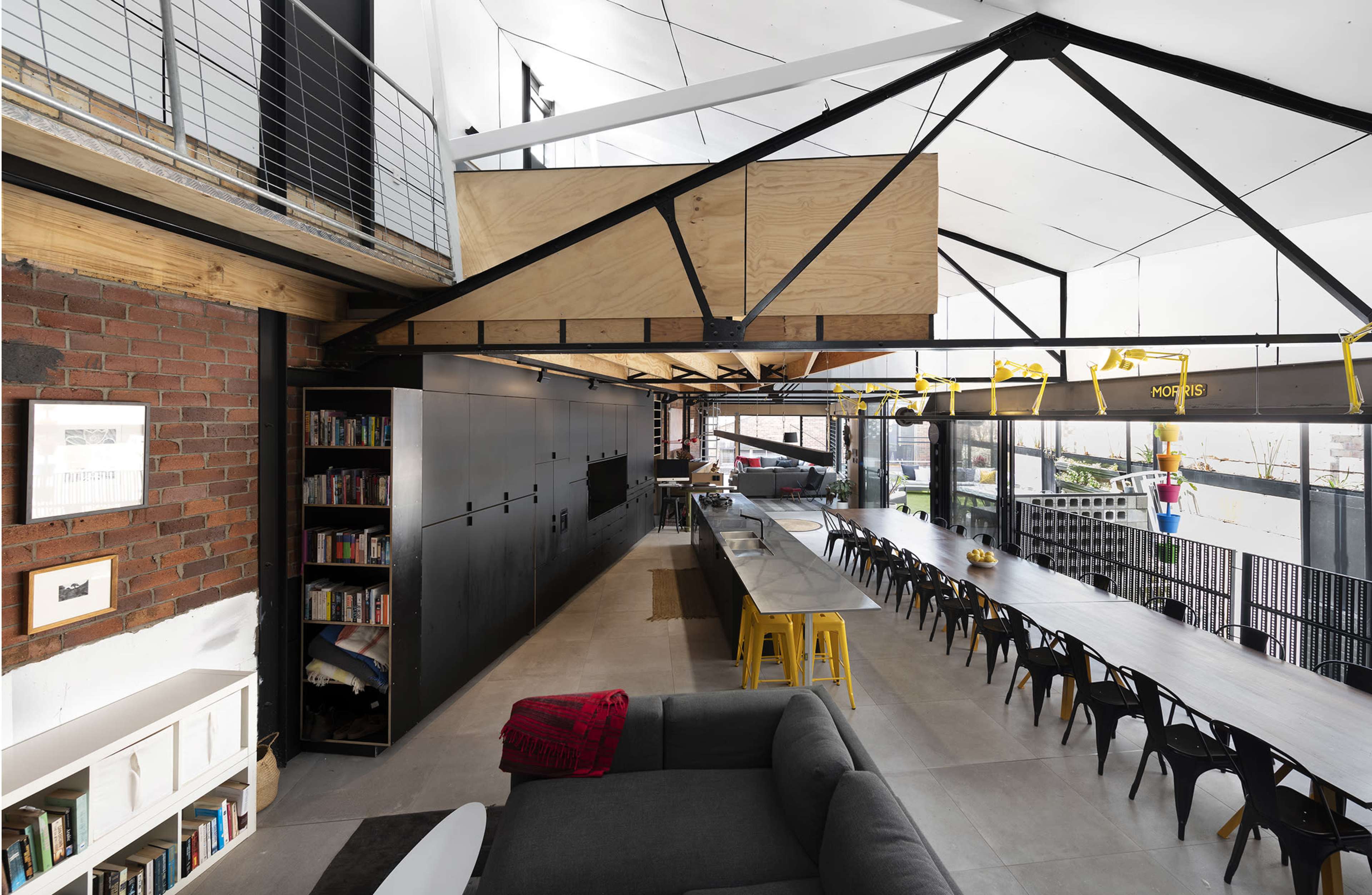 A modern interior space featuring an open-plan kitchen and dining area with a long table, a black wall of cabinetry, and a mix of industrial and contemporary design elements.