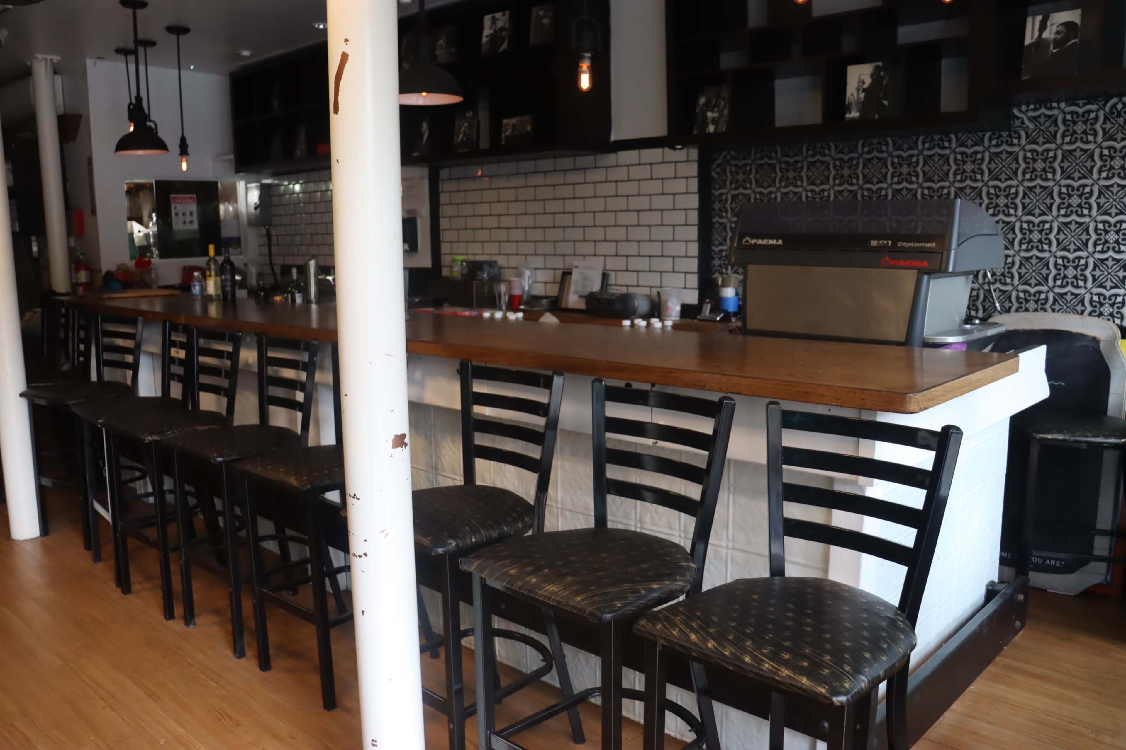 A row of empty black chairs lines a wooden bar counter in a modern café setting.